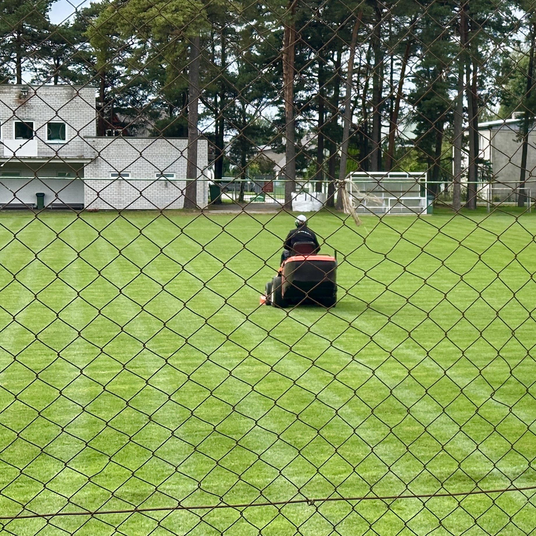 Inimene niidab rohelist põldu punamusta muruniidukiga.