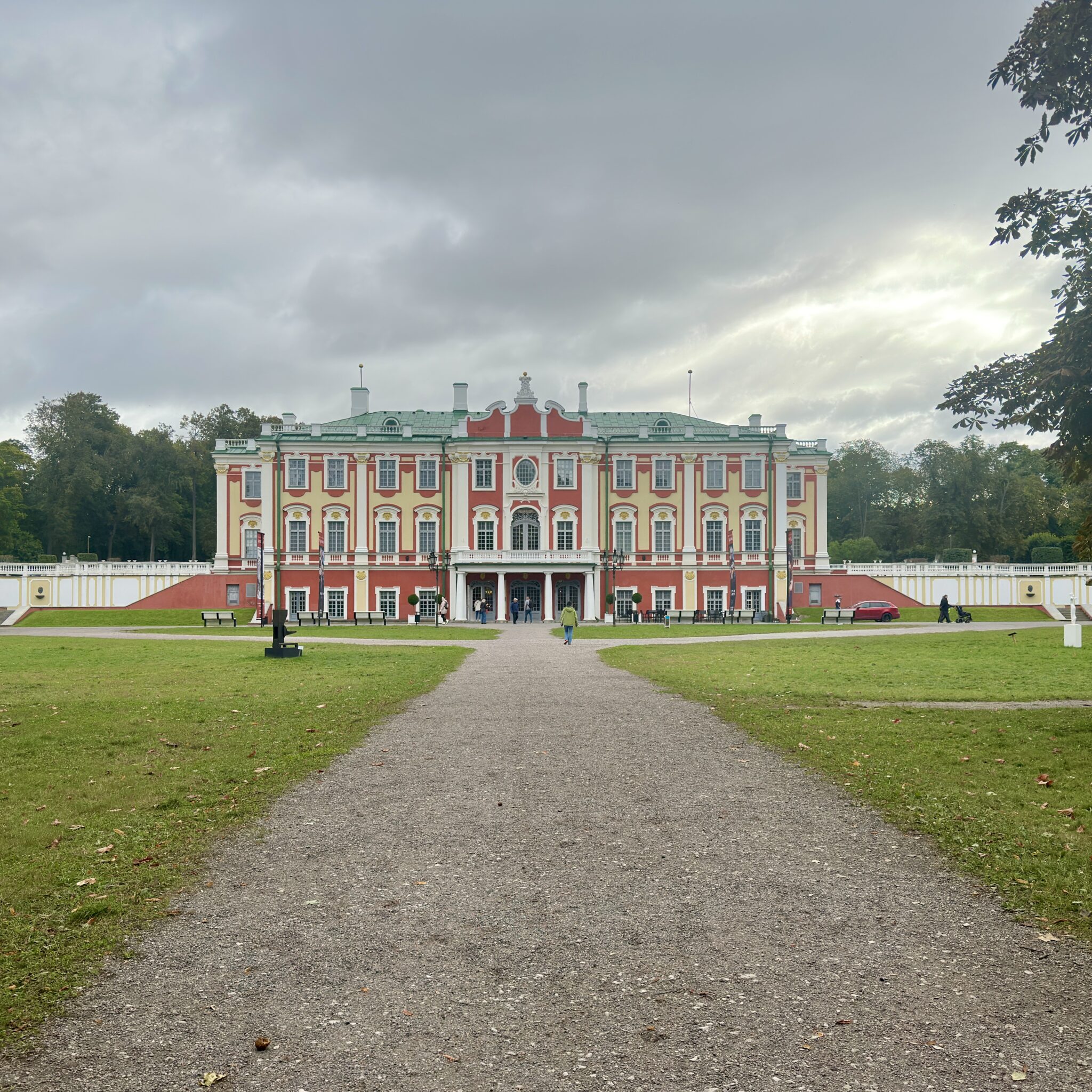 Suur ajalooline hoone punase ja kollase fassaadiga, ümbritsetud rohelusega.