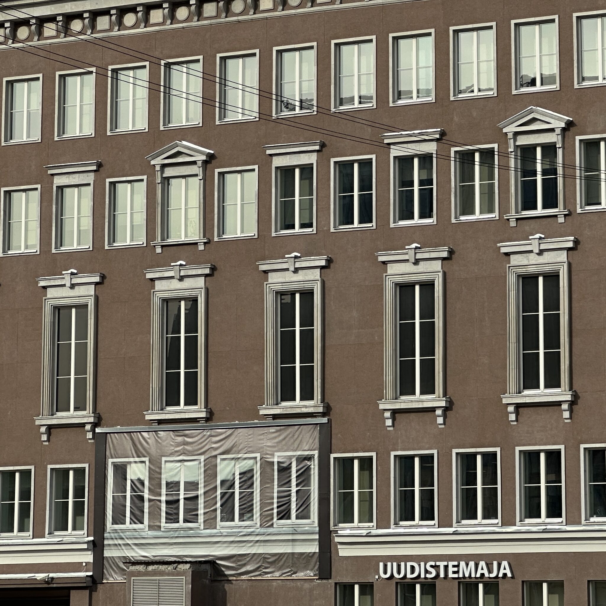 Pruun hoone paljude akendega ja sildiga „UUDISTEMAJA.”