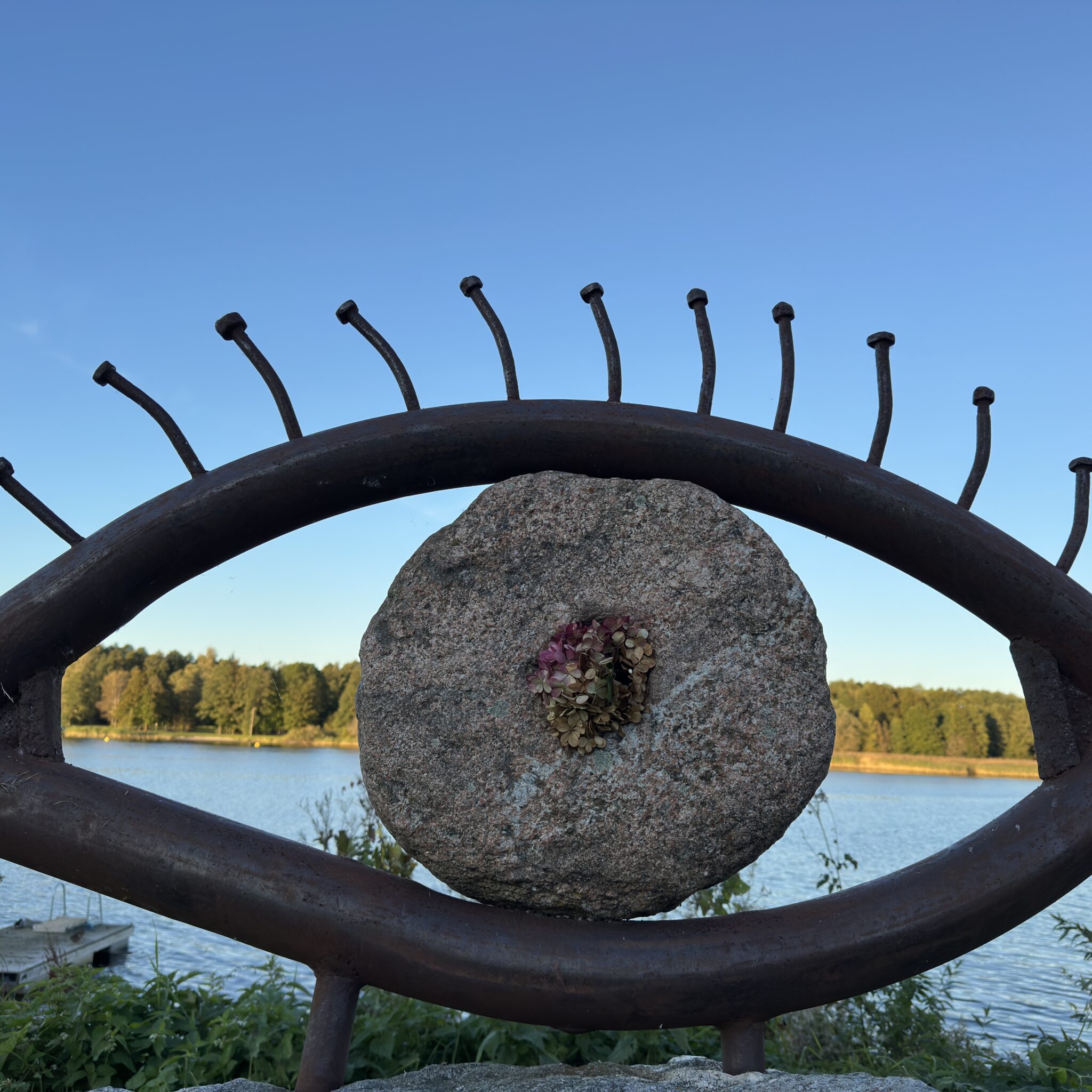 Metallist silmakujuline skulptuur raamib kivi, mille keskel on lill.