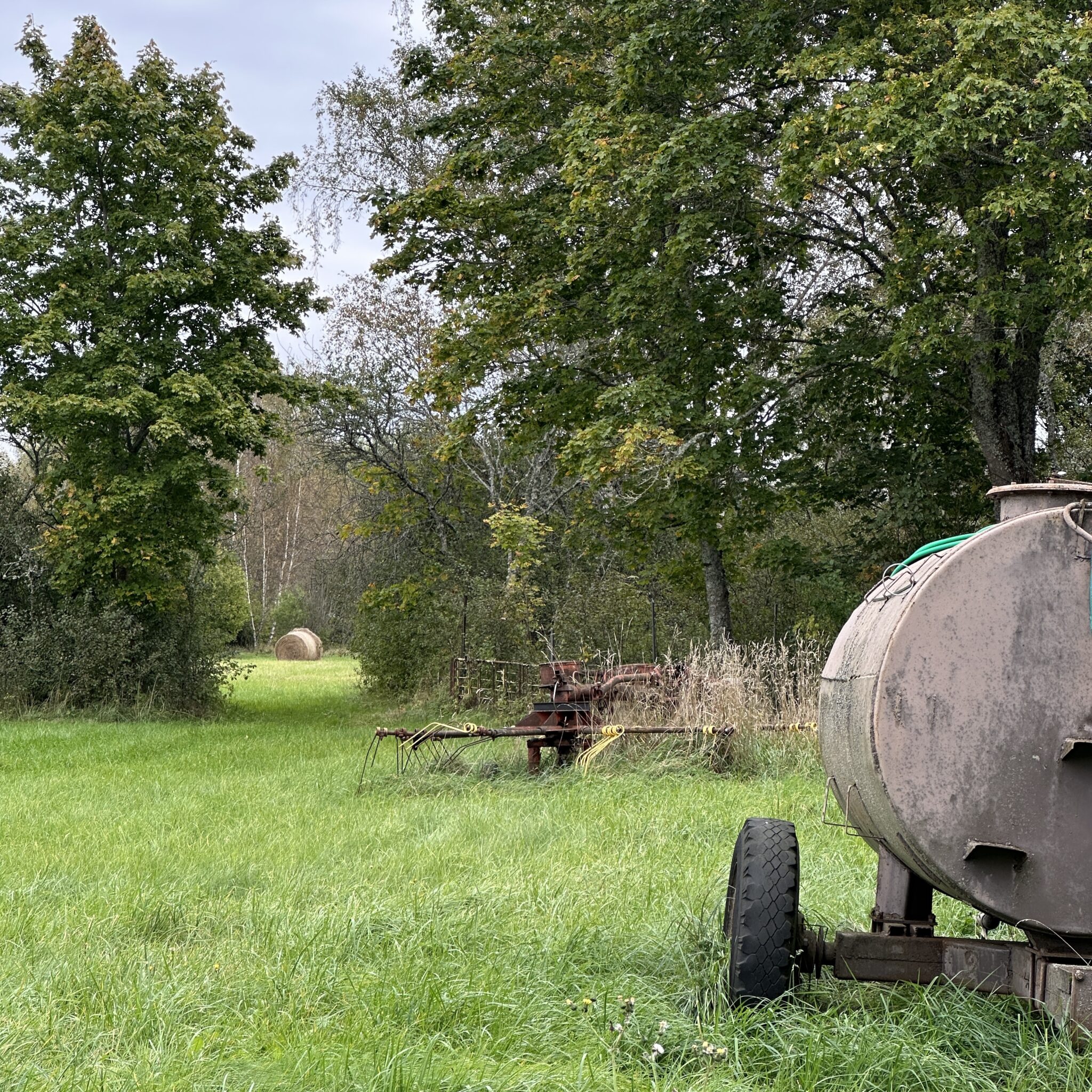 Maastik roostes mahuti ja põllumajandusmasinatega rohelisel põllul.