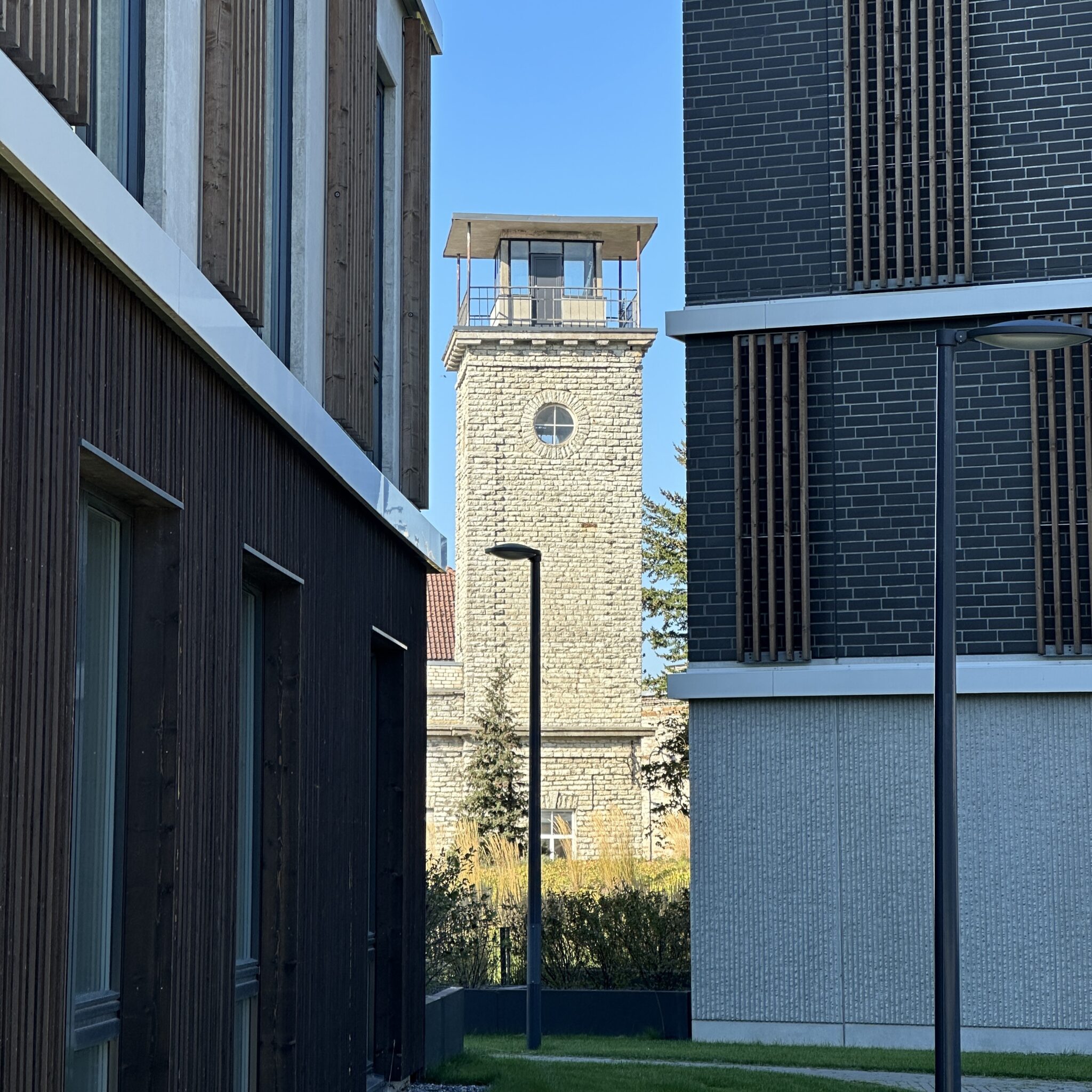 Kellatorn seisab kaasaegsete hoonete vahel, taustal selge sinine taevas.