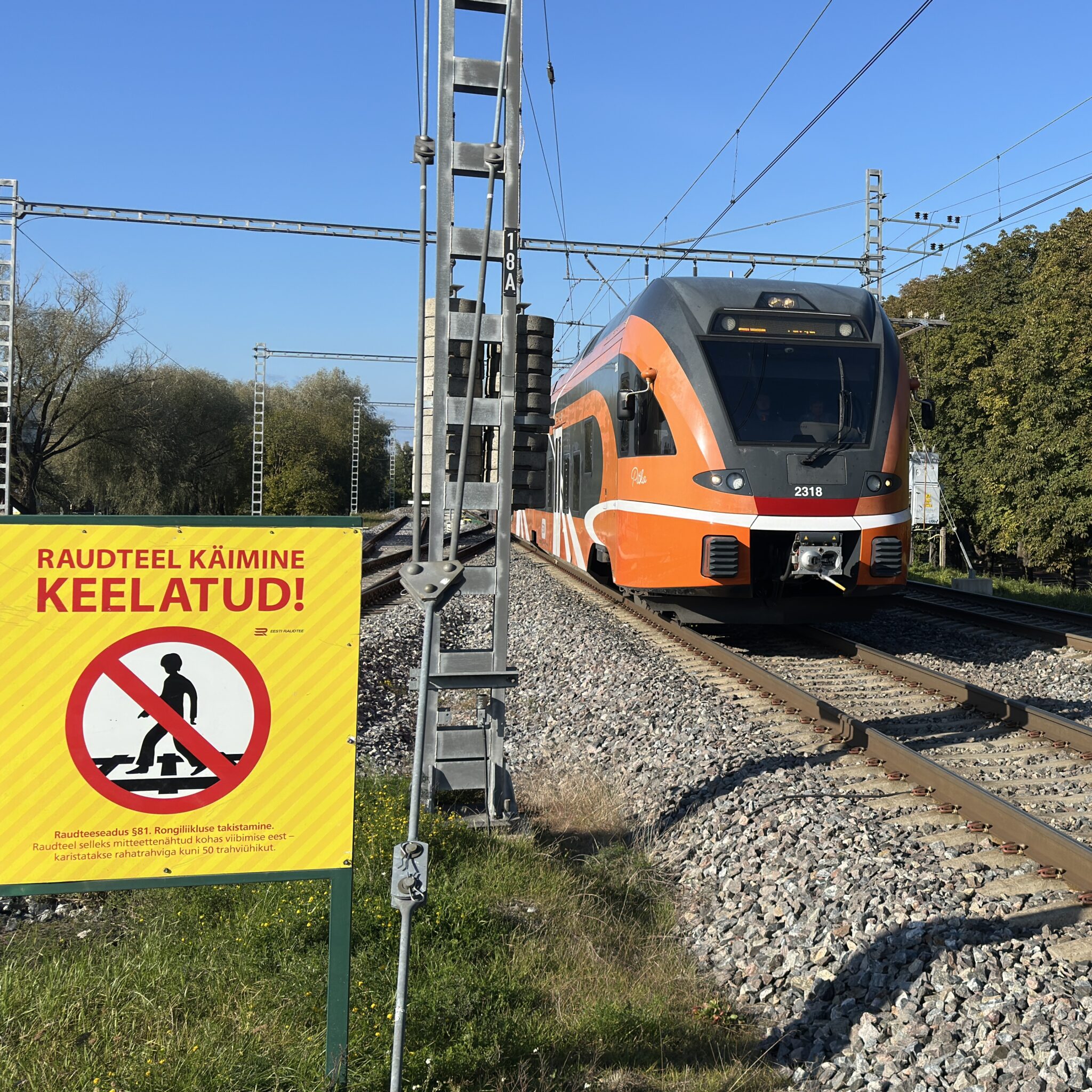 Oranž rong rööbastel, kõrval silt jalakäijate keeluga.