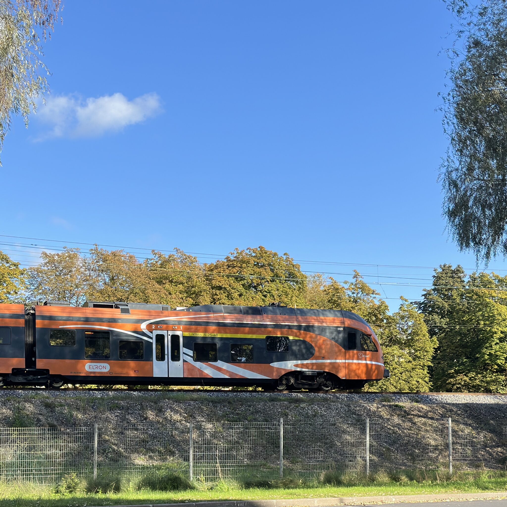 Oranž rong rööbastel, sinine taevas ja puud.