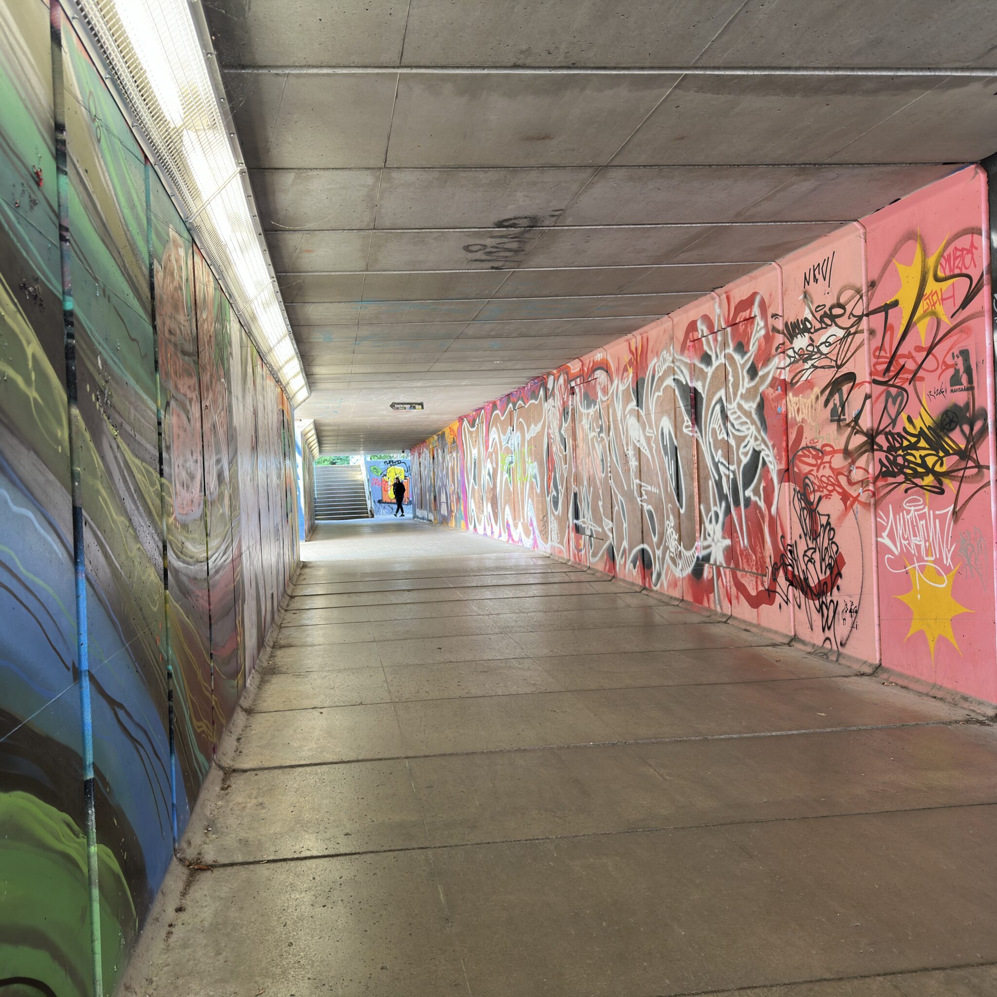 Värviline grafitiga tunnel, millest kõnnib läbi inimene.