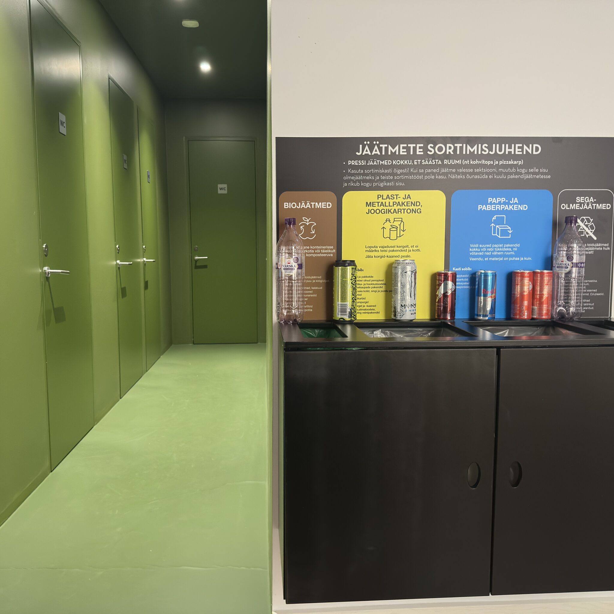 Taaskasutusjaam erinevate jäätmeliikide konteineritega rohelises koridoris.