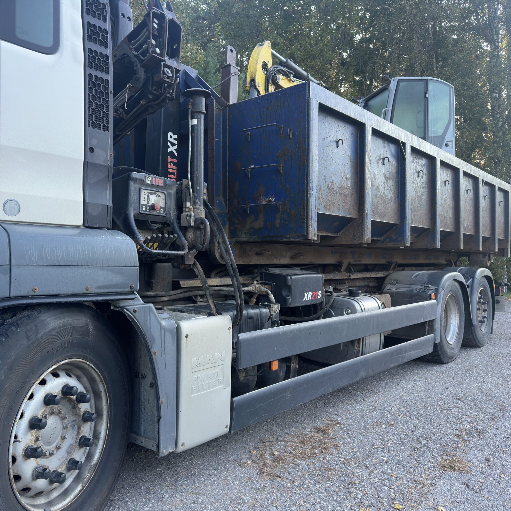 Suur kallurauto hüdrotõstukiga pargitud metsaalal.