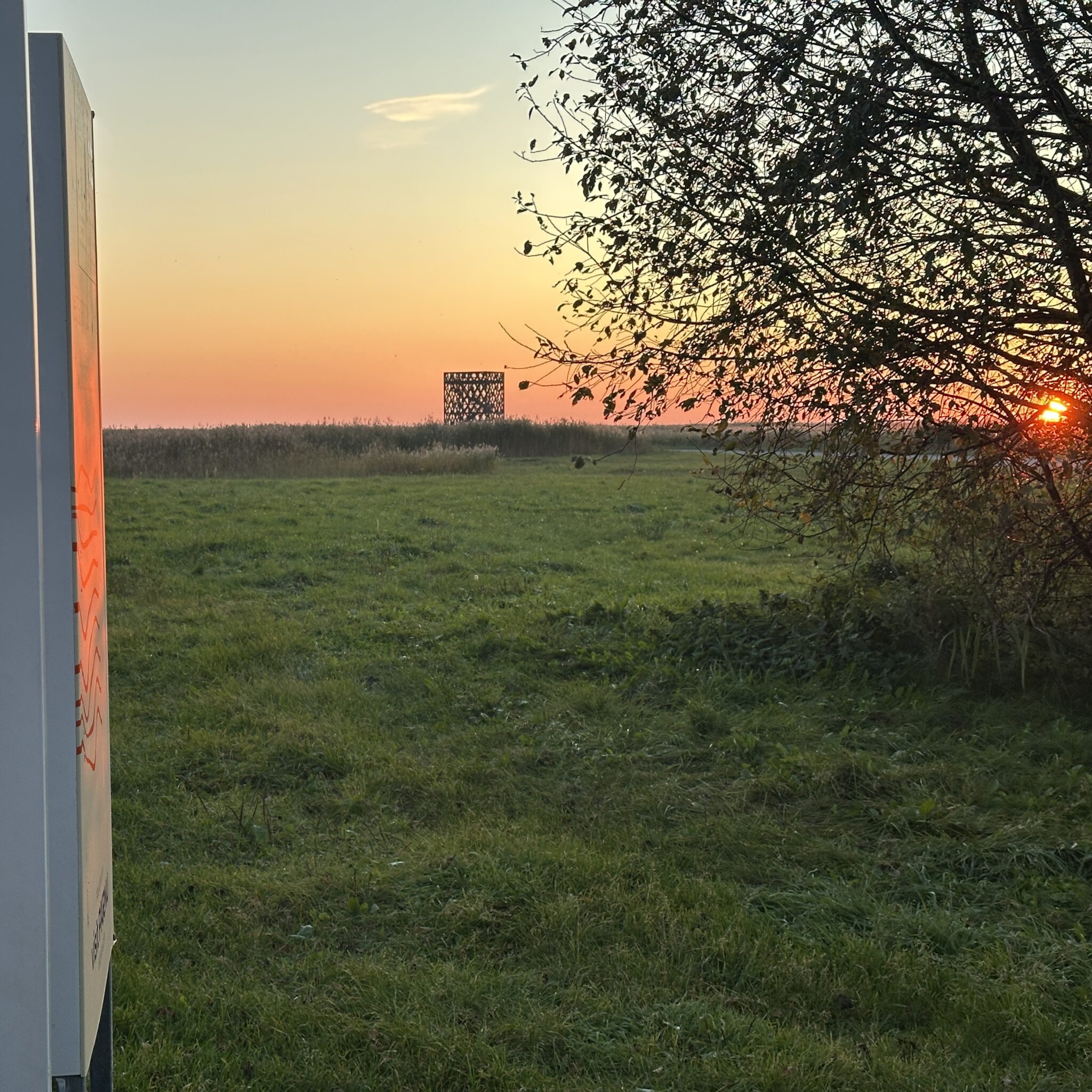 Päikeseloojang rohumaal, kauguses kaasaegne ehitis.