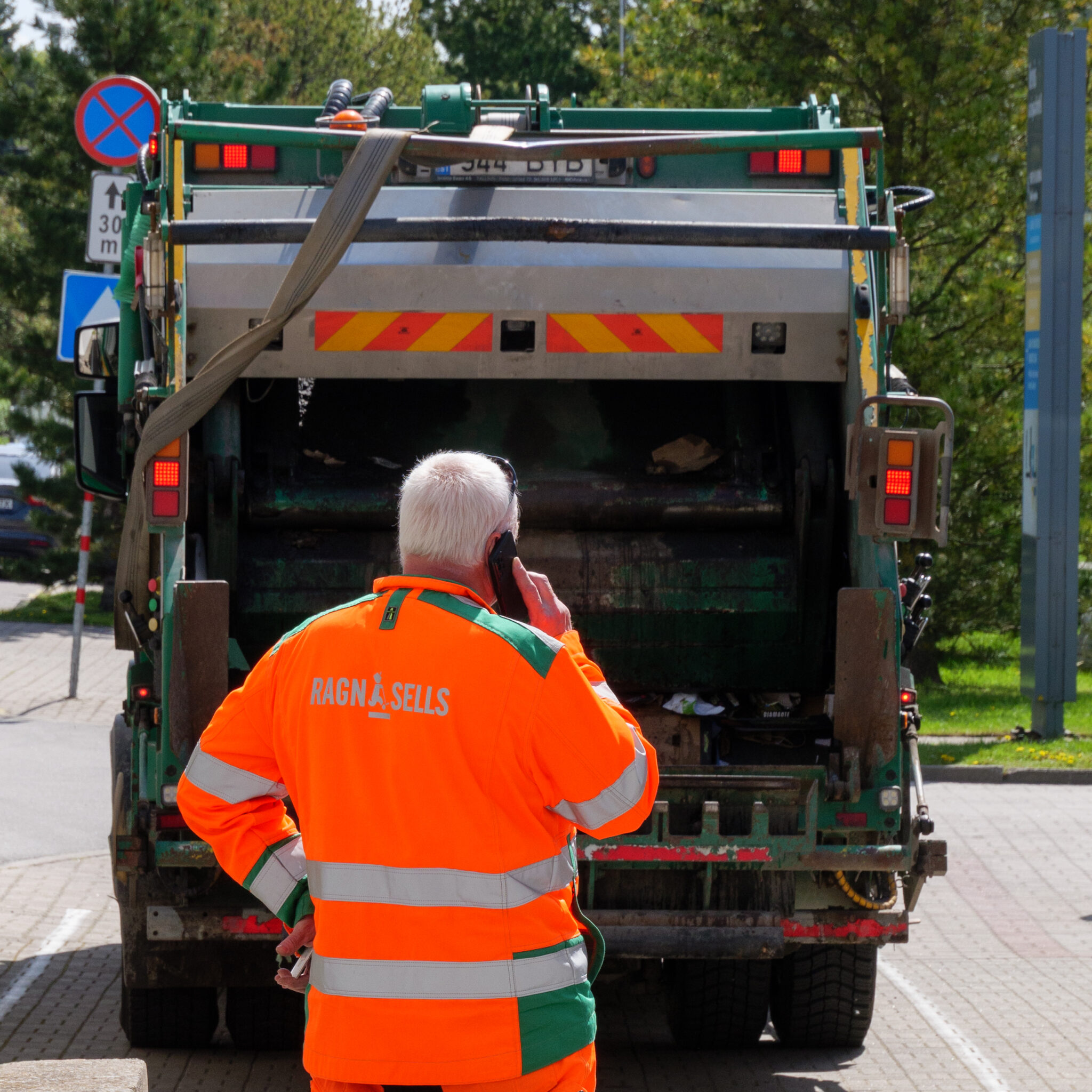 Prügiautojuht räägib telefoniga prügiauto kõrval.