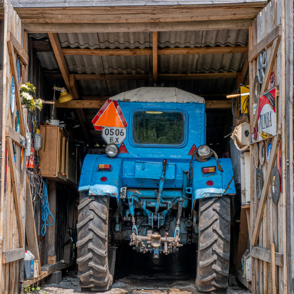 Sinine traktor maalähedases töökojas puidust seinte ja plekk-katusega.