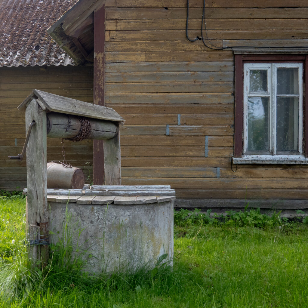 Vana puust kaev metallämbriga ja aknaga maalähedases majas.