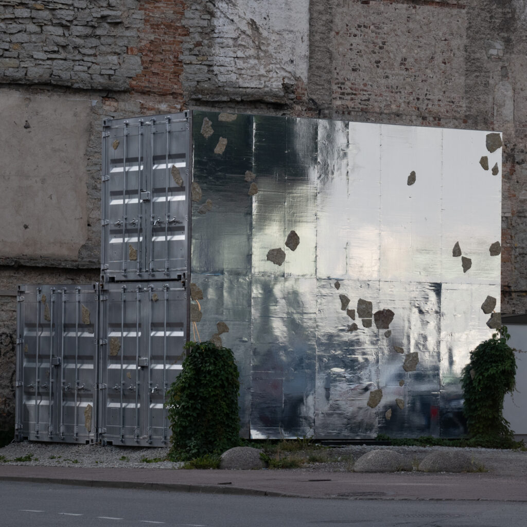 Kaks metallkonteinerit ja peegeldav sein kulunud seina taustal.