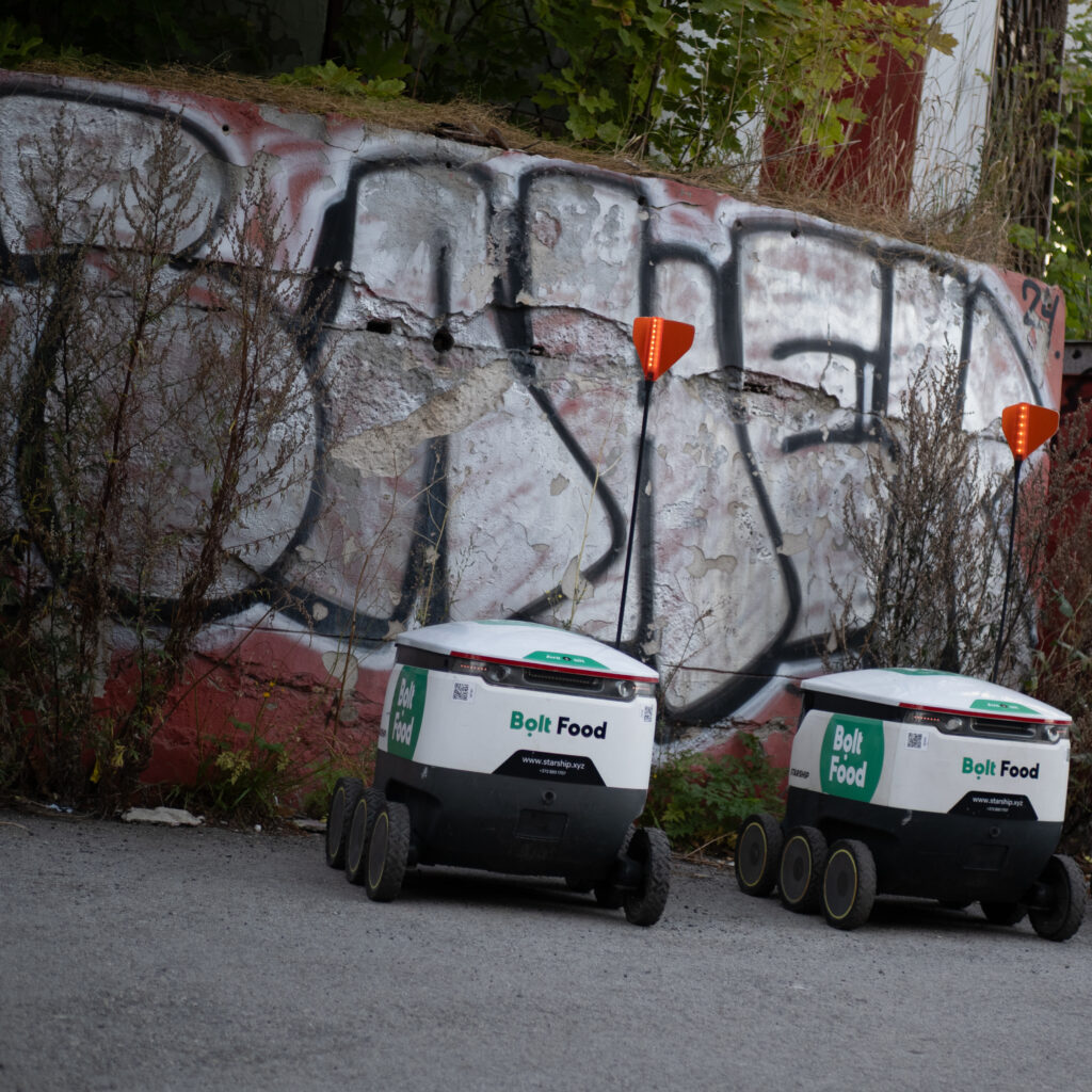 Kaks Bolt Foodi tarneroboti graffitidega kaetud seina ees.