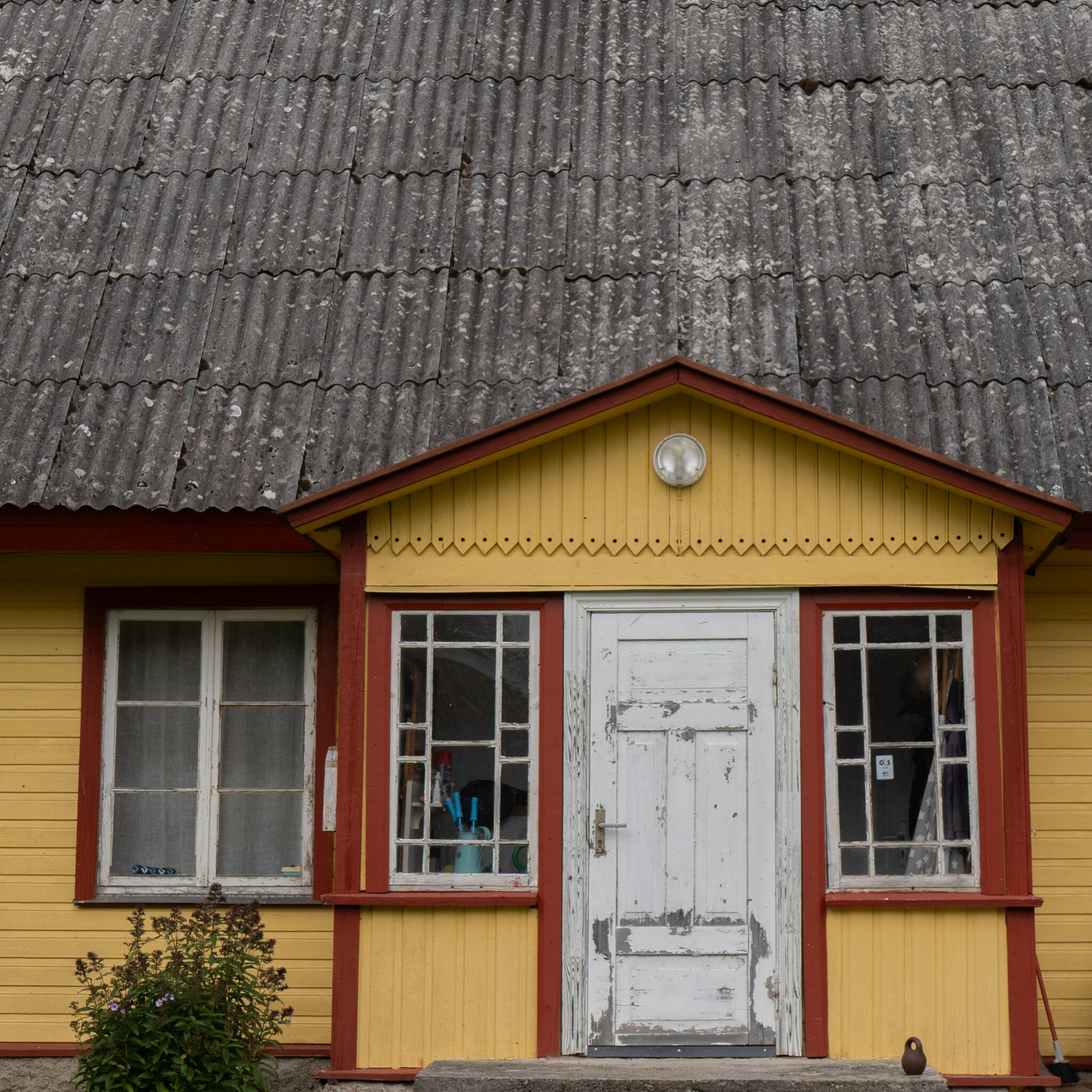 Kollane ja punane maja lainelise plekk-katusega.