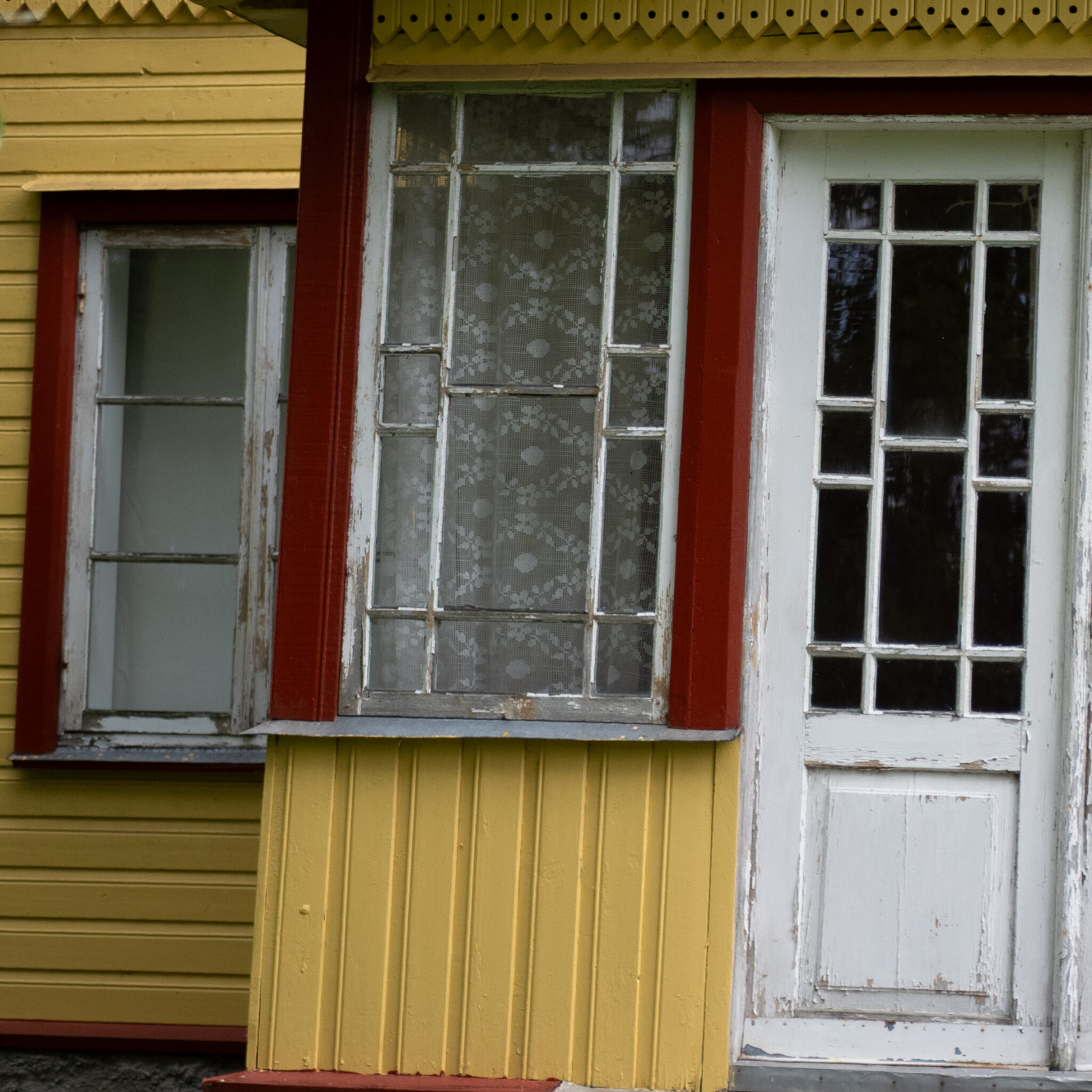 Kollane maja punaste äärte ja pitskardinate taga.