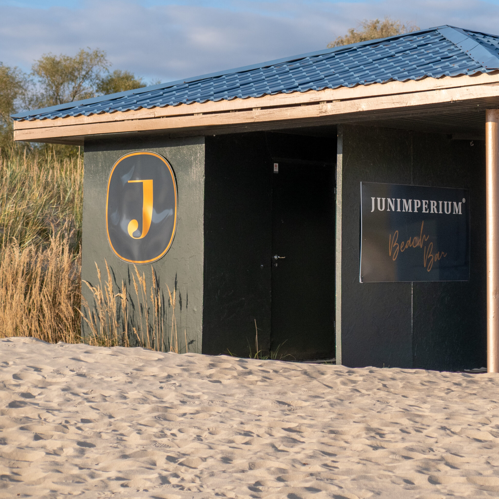 Rannamajake Junimperiumi logoga ja sildiga „Beach Bar”.