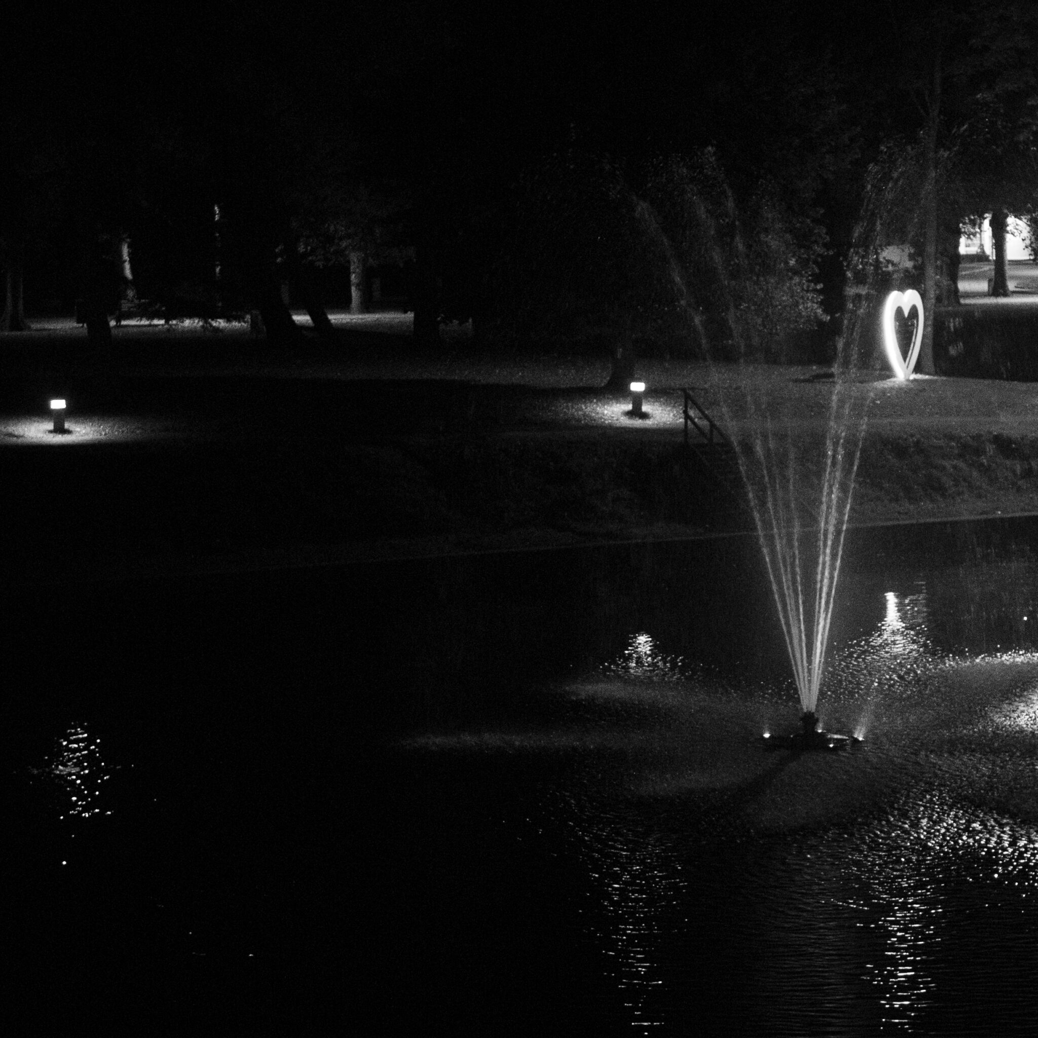 Süda-kujulise valgusega purskkaev öises tiigis.