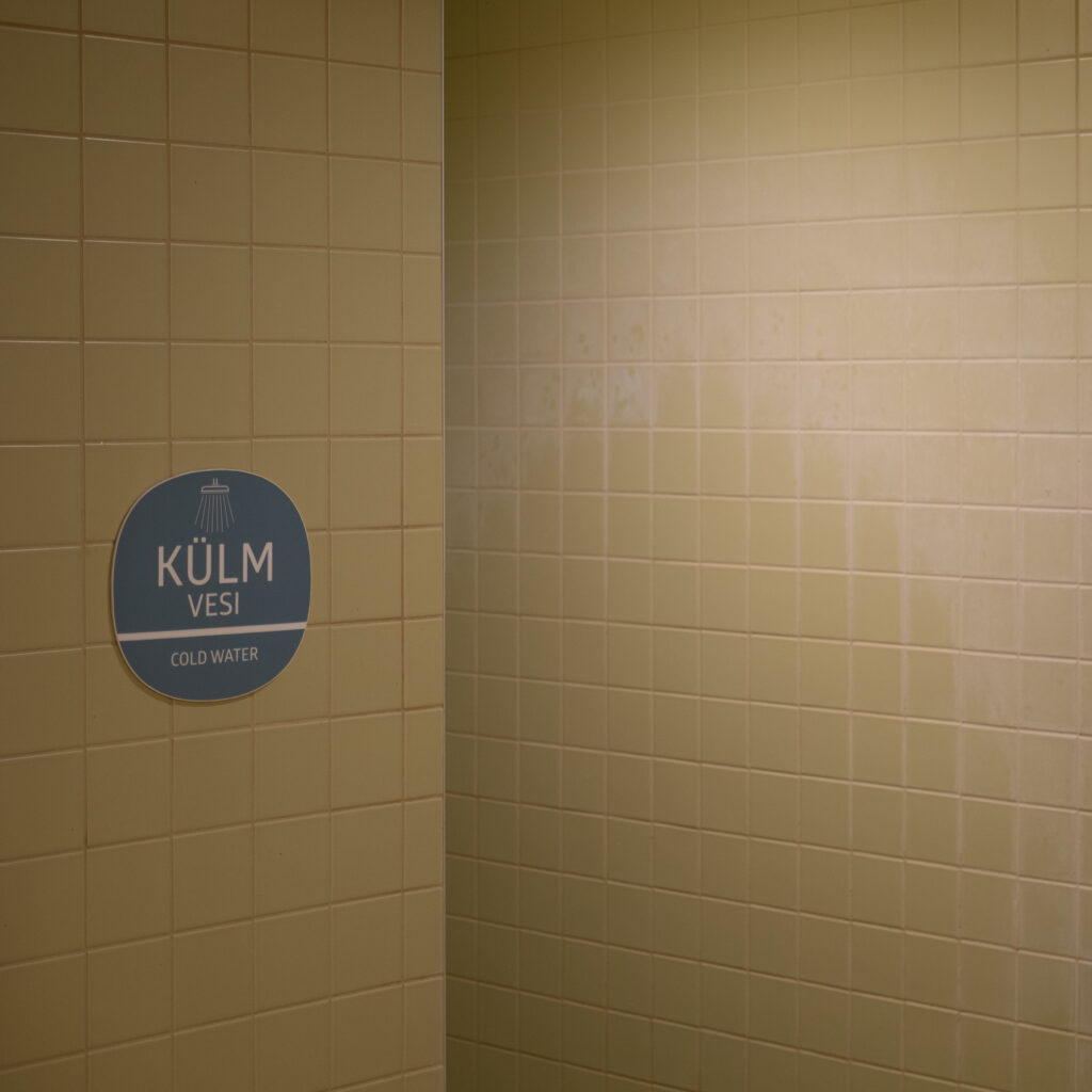 Sinine silt kirjaga „KÜLM VESI” vannitoas kollaste plaatidega.