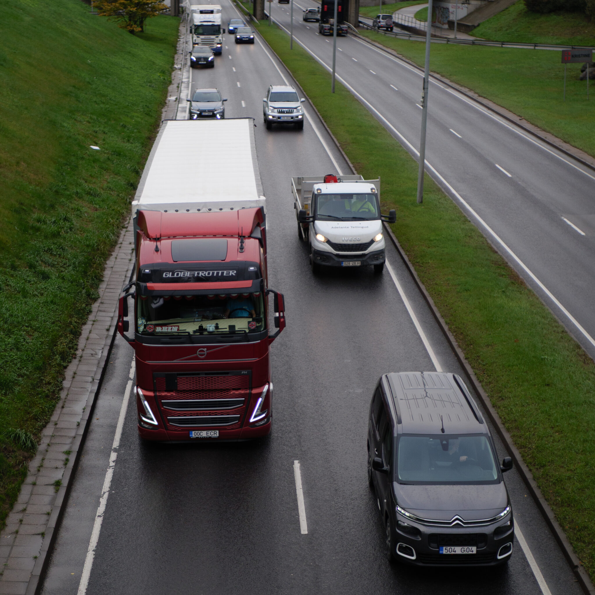 Punane veoauto märjal teel, taga valge rekka ja auto.