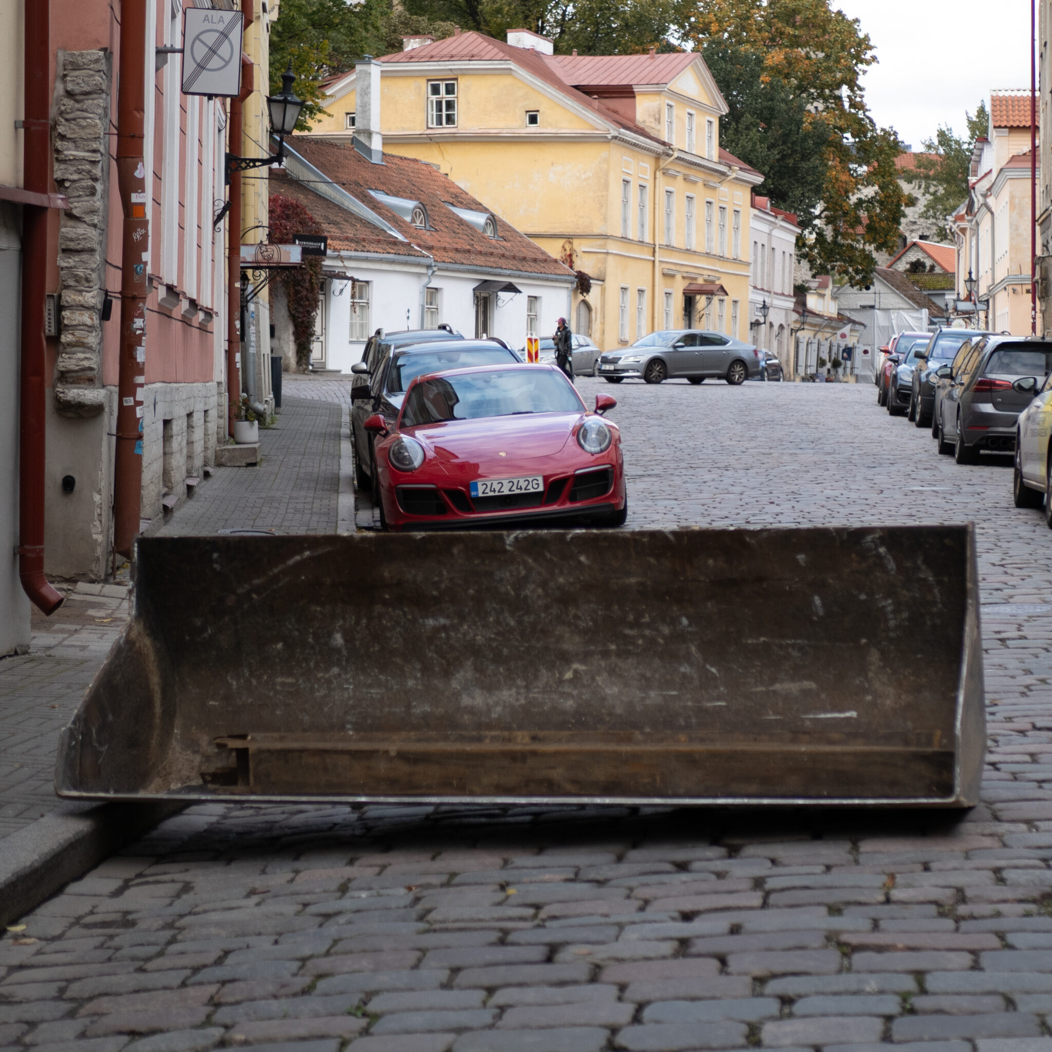 Punane Porsche sillutatud tänaval suure metallkopaga taustal.