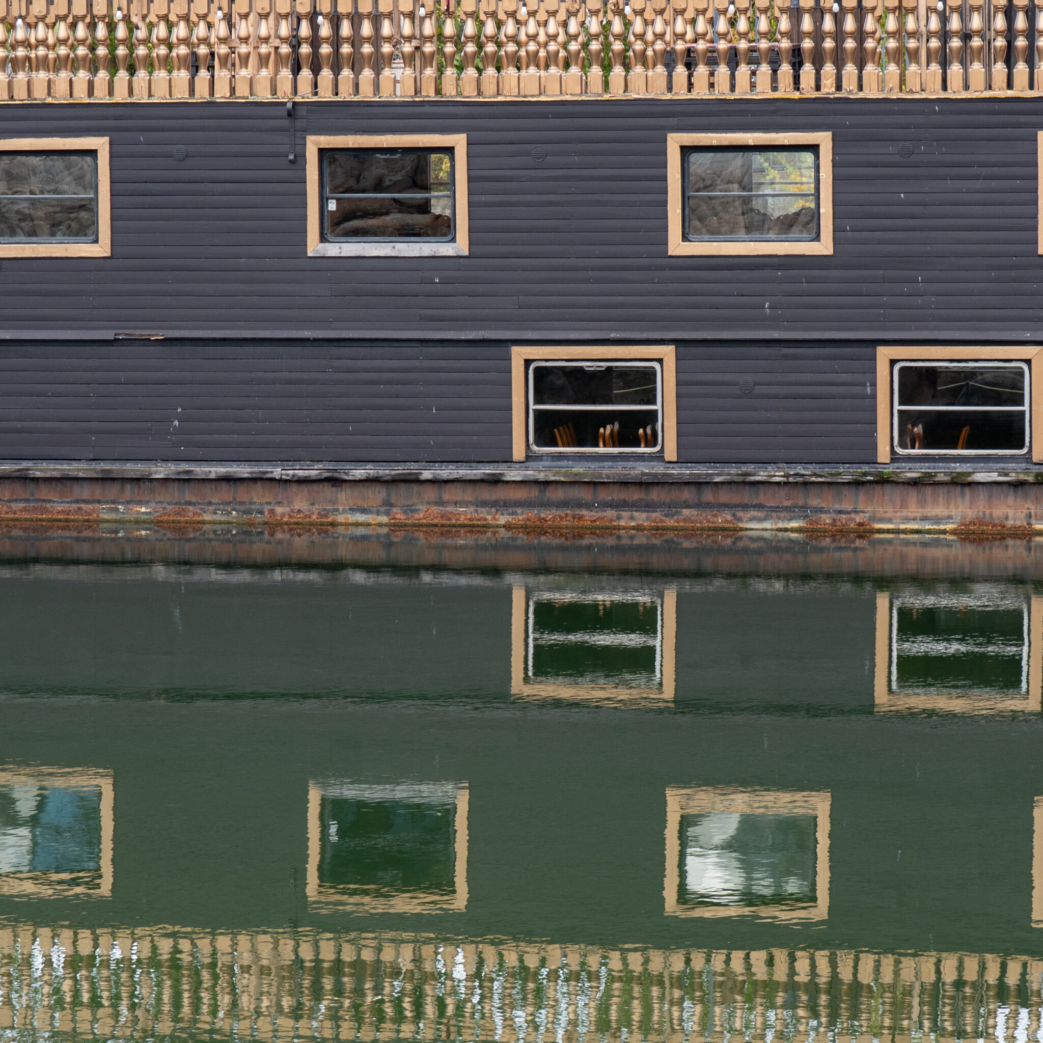 Must hoone akendega ja puidust aiaga peegeldub vees.