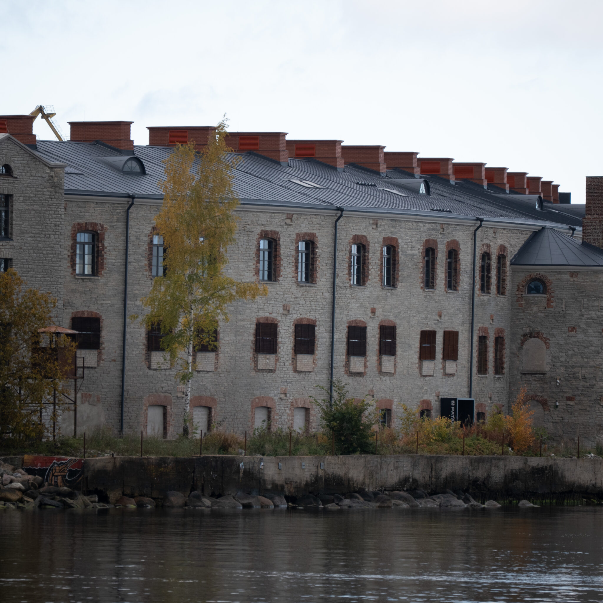Ajalooline tellis- ja kivimüüridega hoone punaste korstnate ja puuga veepiiril.
