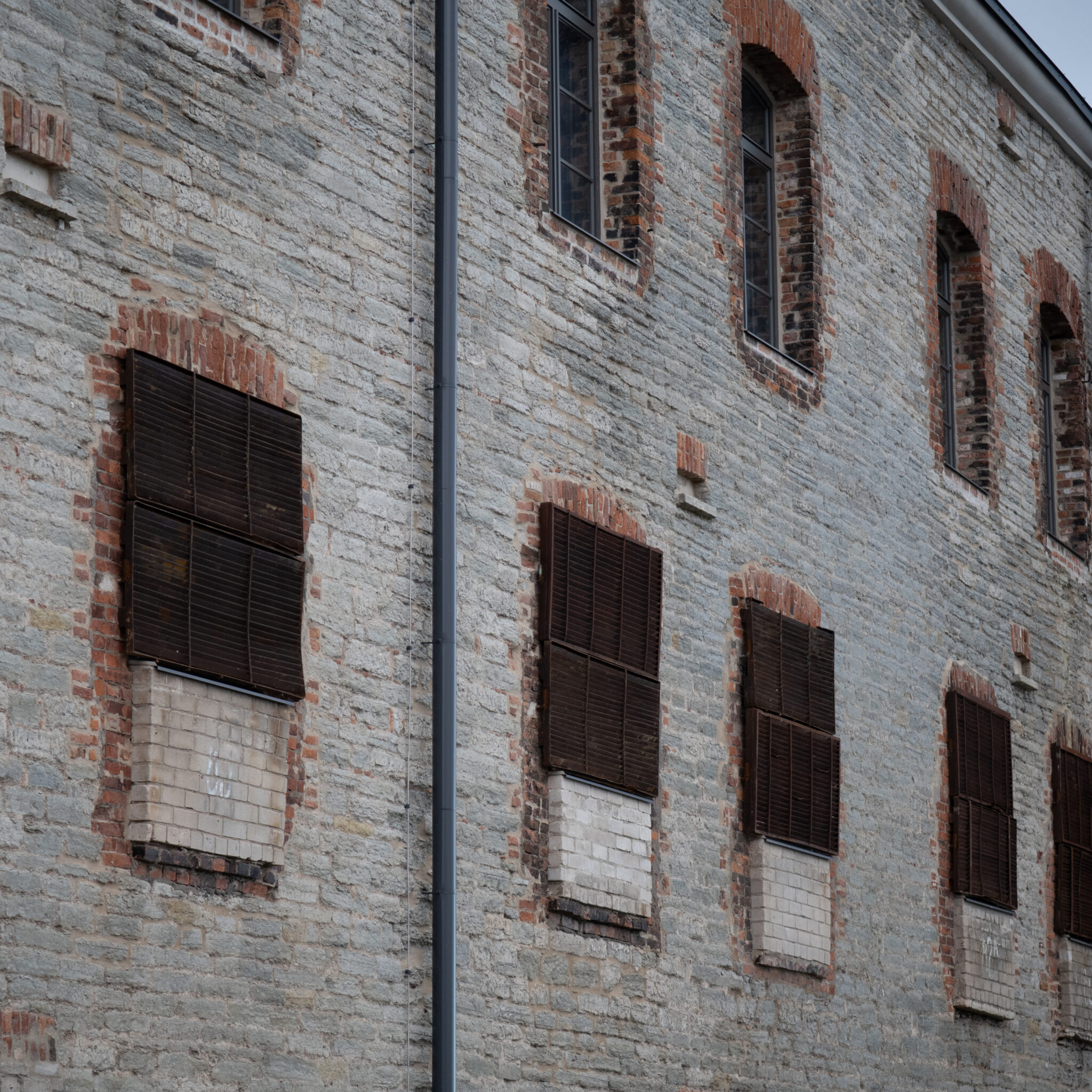 Ilmastikust kulunud tellishoone kaarjate akende ja metalltoruga küljel.