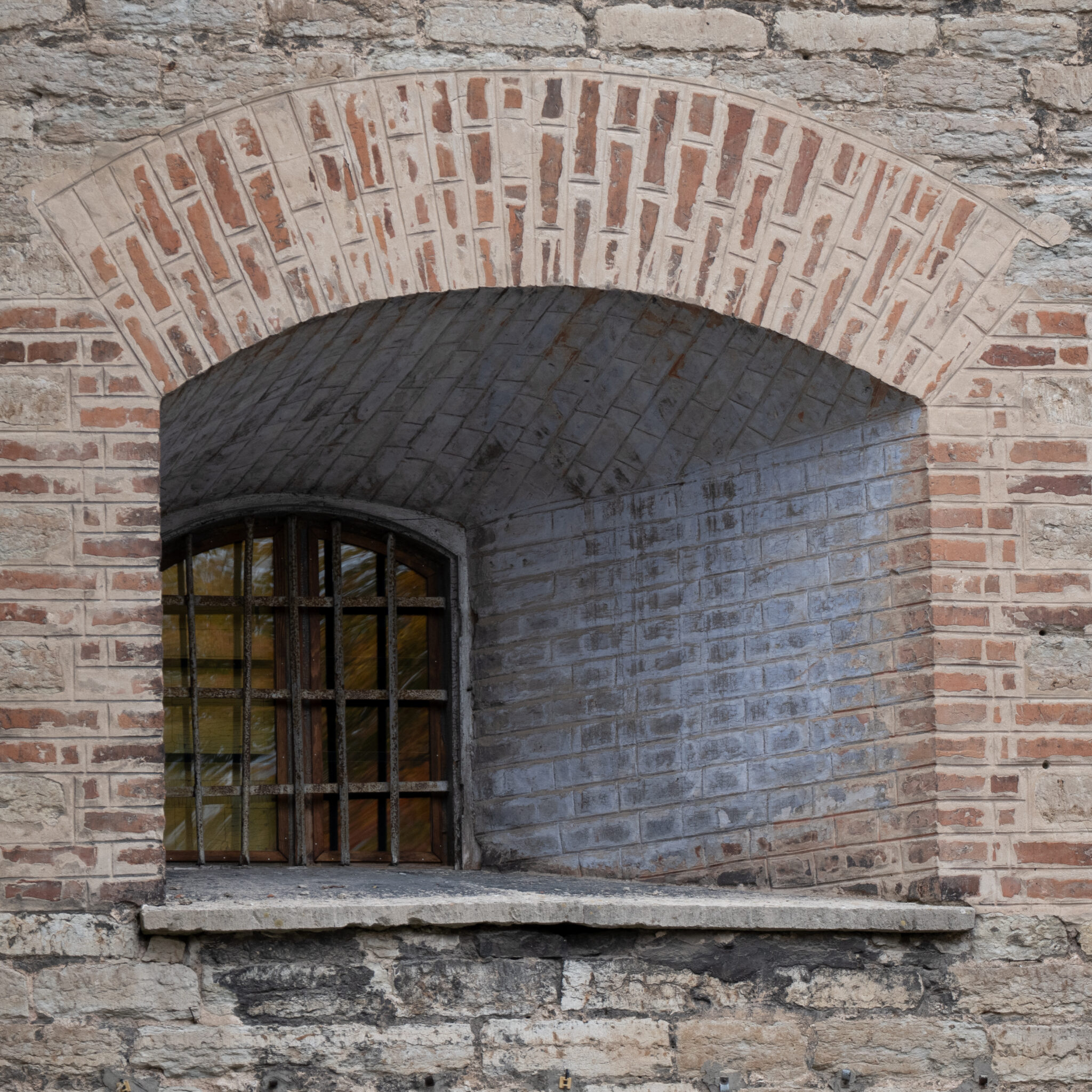 Kaarjas aken metallvõrega tellisseinas.