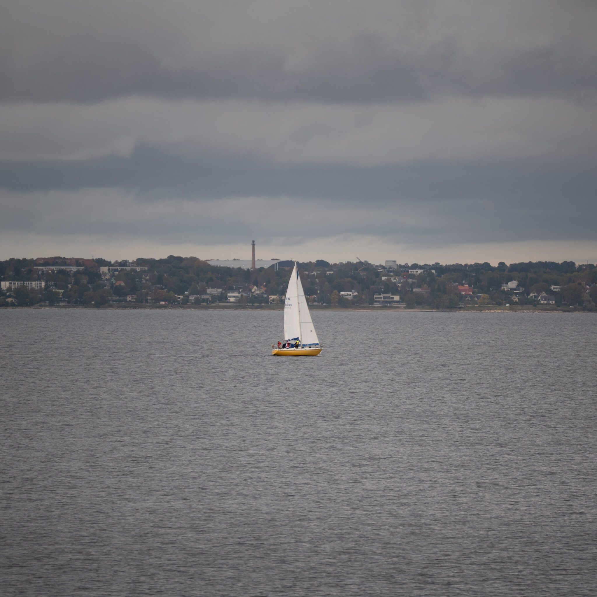 Purjekas rahulikul veel kauge linnasiluetiga taustal.