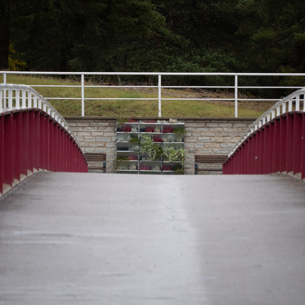 Punane-valge sild viib kiviseinani, mida katab rohelus.