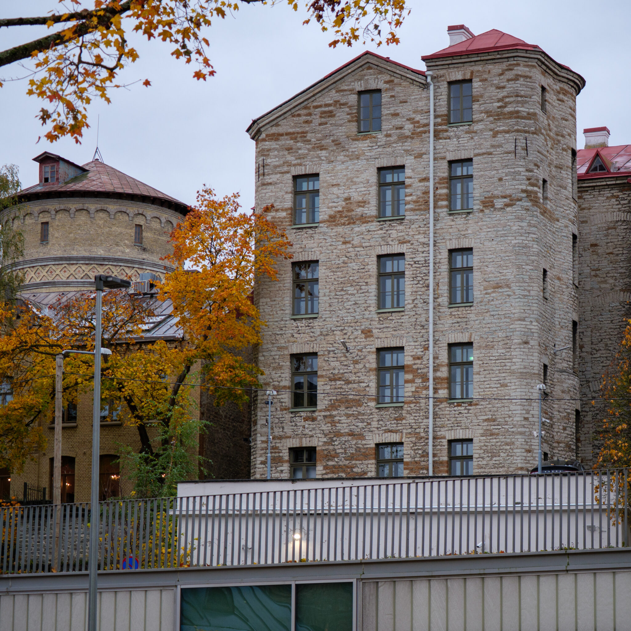 Ajalooline punase katuse ja ümara torniga hoone sügislehtede keskel.