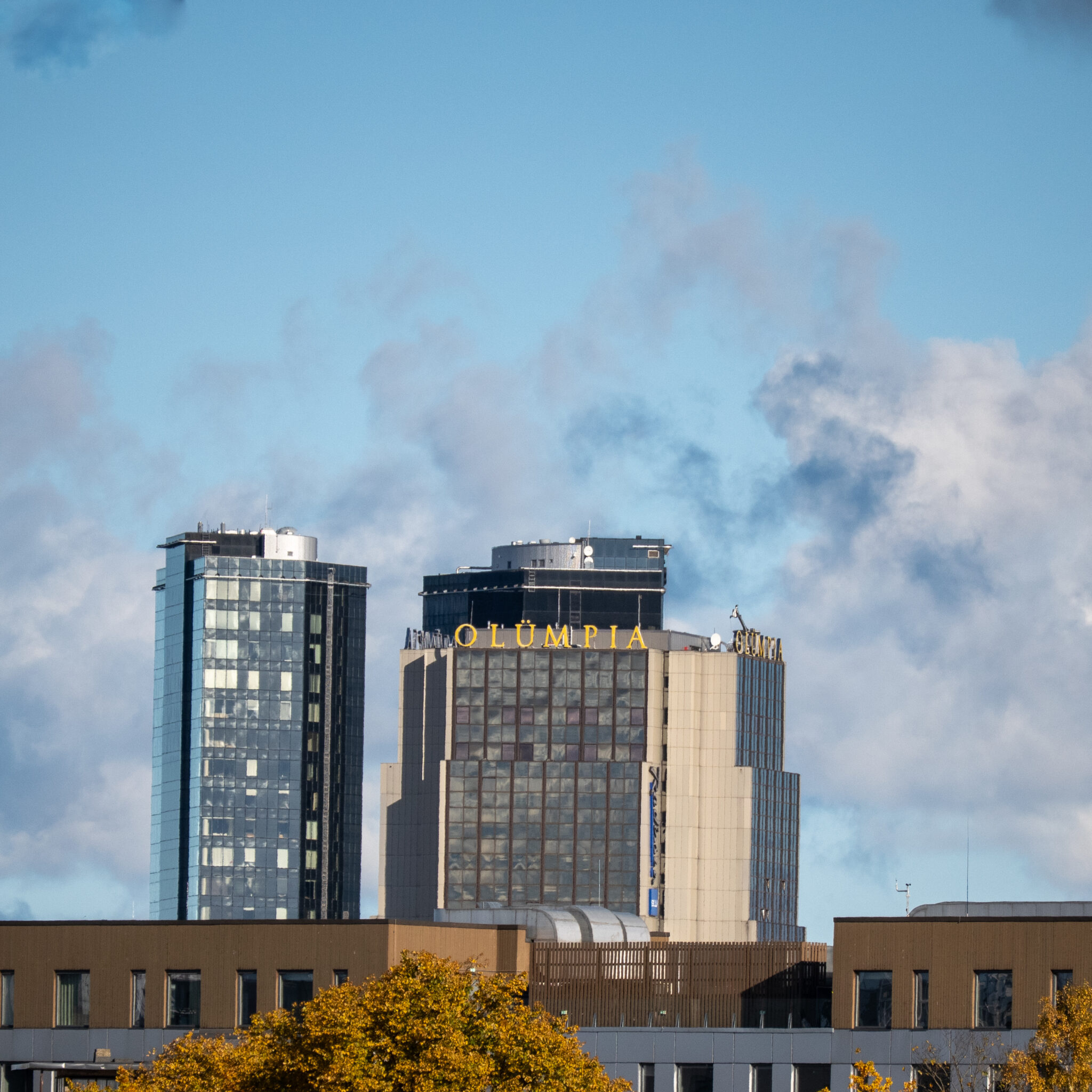 Kaks kõrget hoonet, üks OLÜMPIA sildiga, sinise pilvise taeva all.