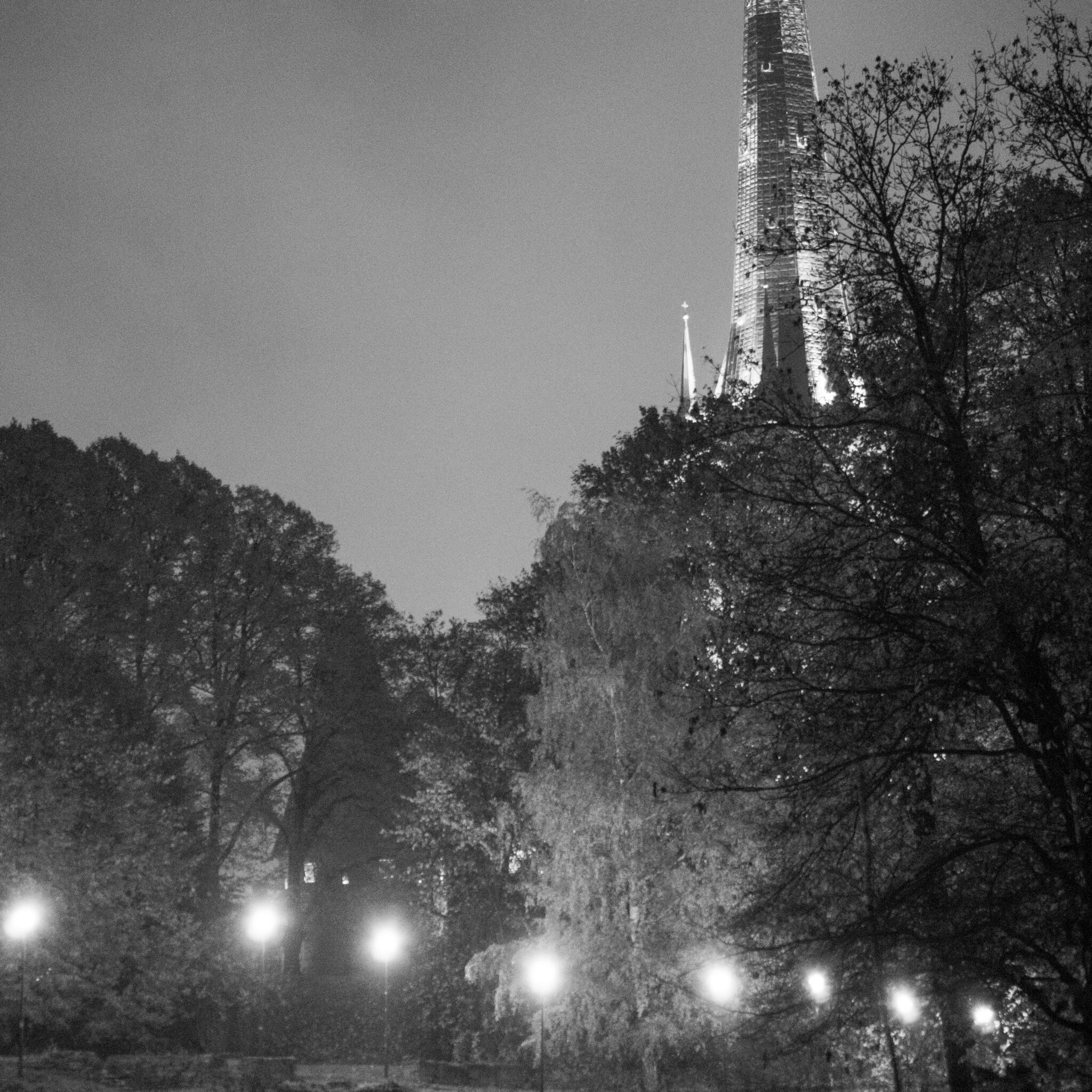 Kirikutorn kõrgub puude vahel, öösel valgustatud.