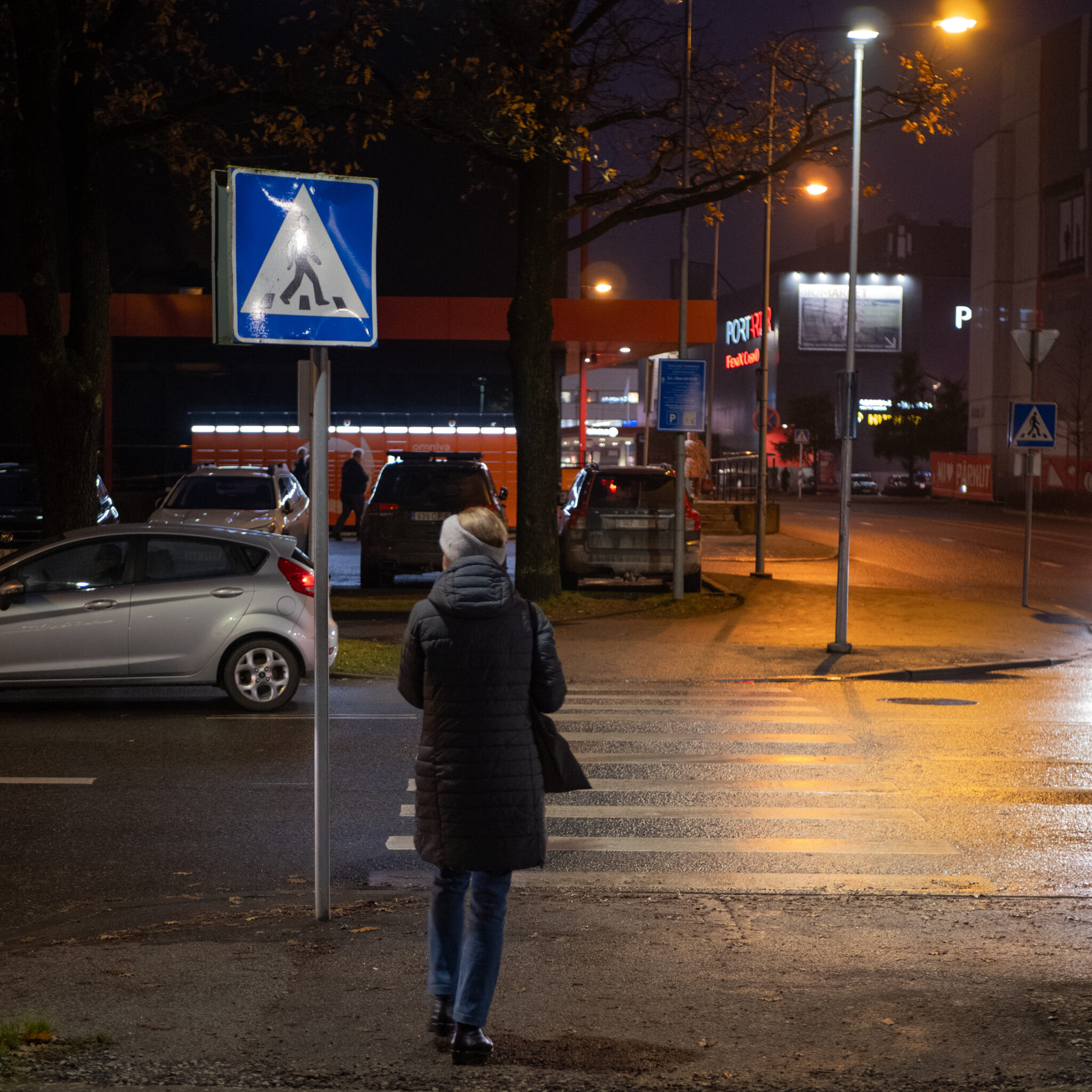 Mustas mantlis naine ületab öisel tänaval teed.