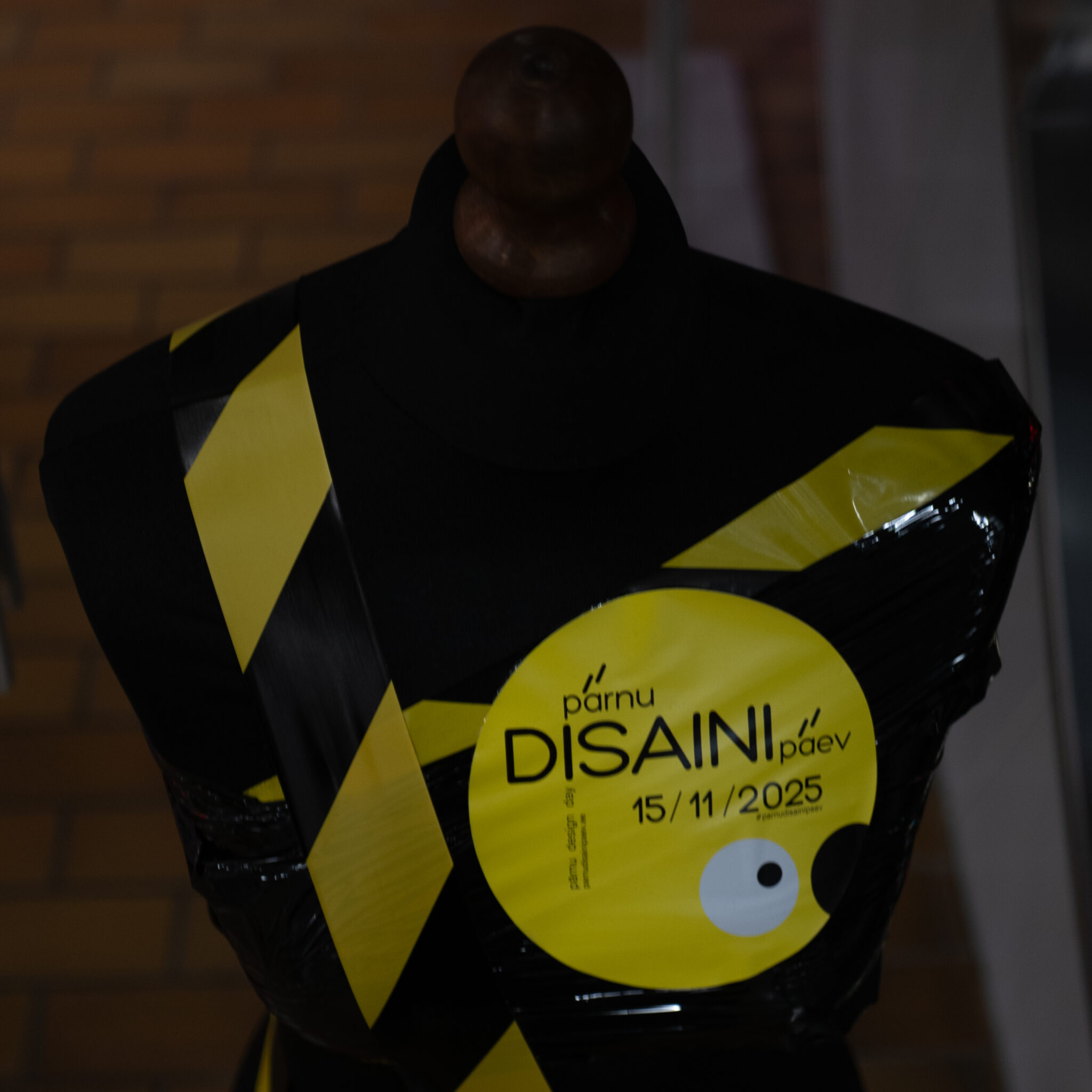 Kollaste ja mustade triipudega mannekeen ning Disaini Design Day 2025 silt.