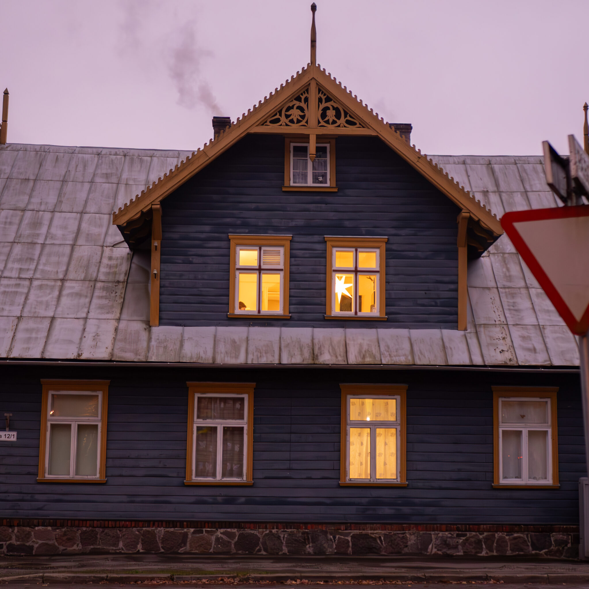 Põlevate akende ja korstnaga maja õhtuhämaruses.