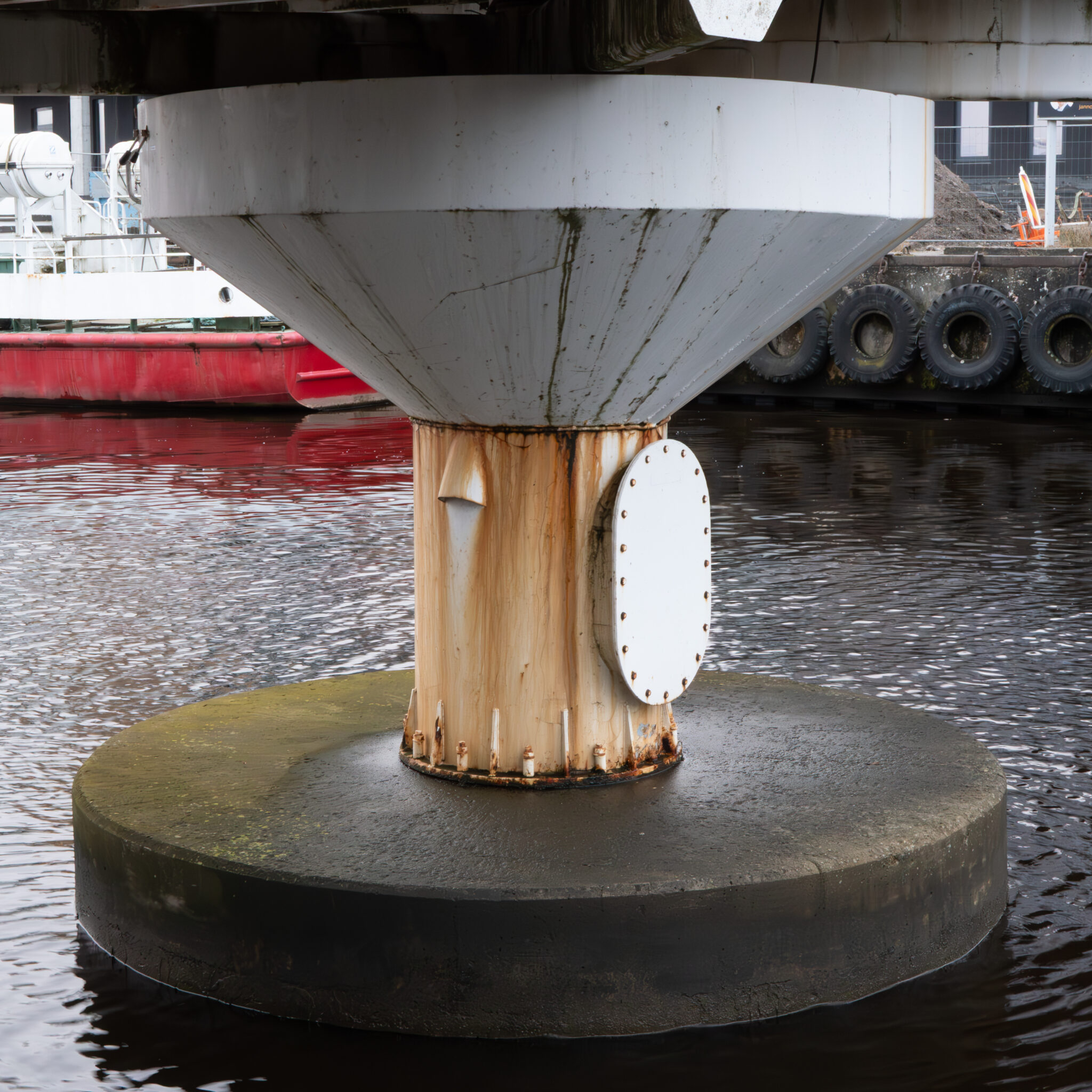 Veekogus asuv roostes valge silindrikujuline rajatis suure valge ümmarguse plaadiga.