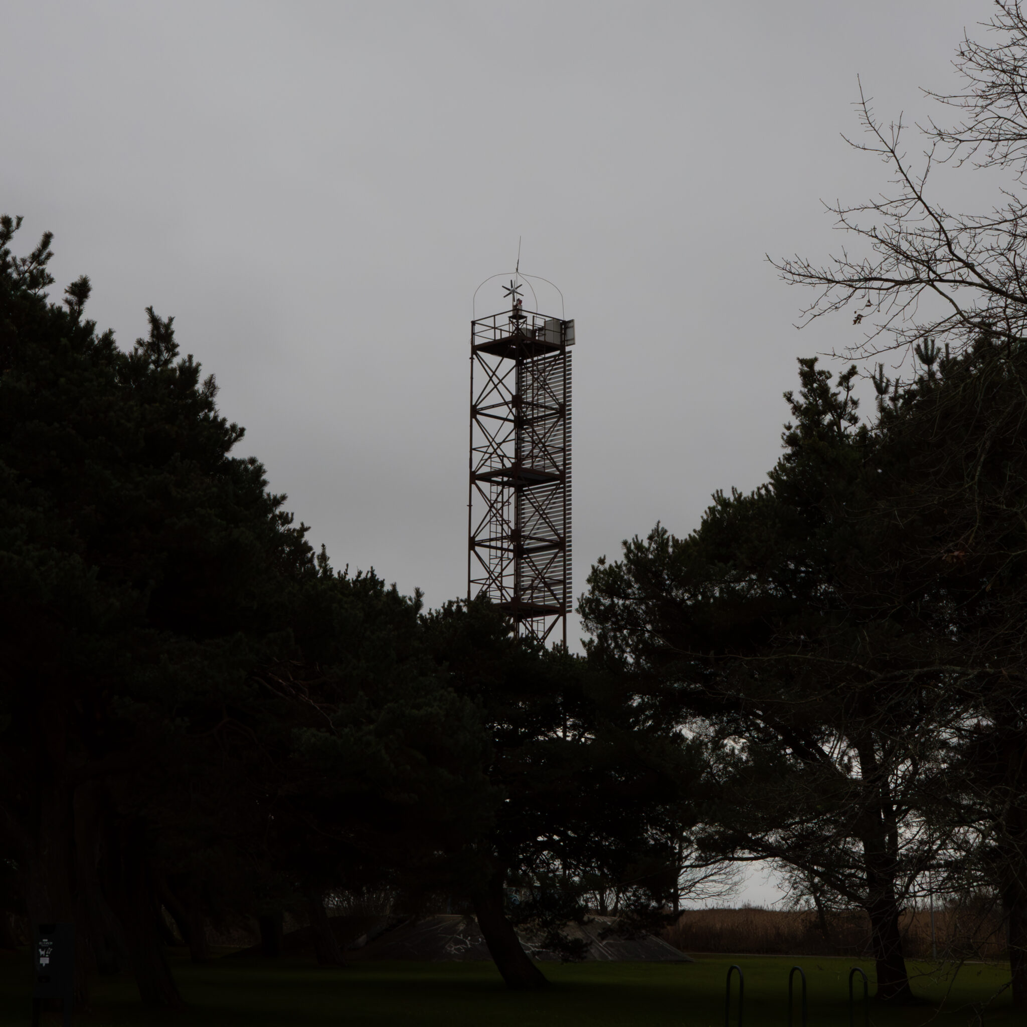 Kõrge tume torn puude vahel pilvise taeva all.
