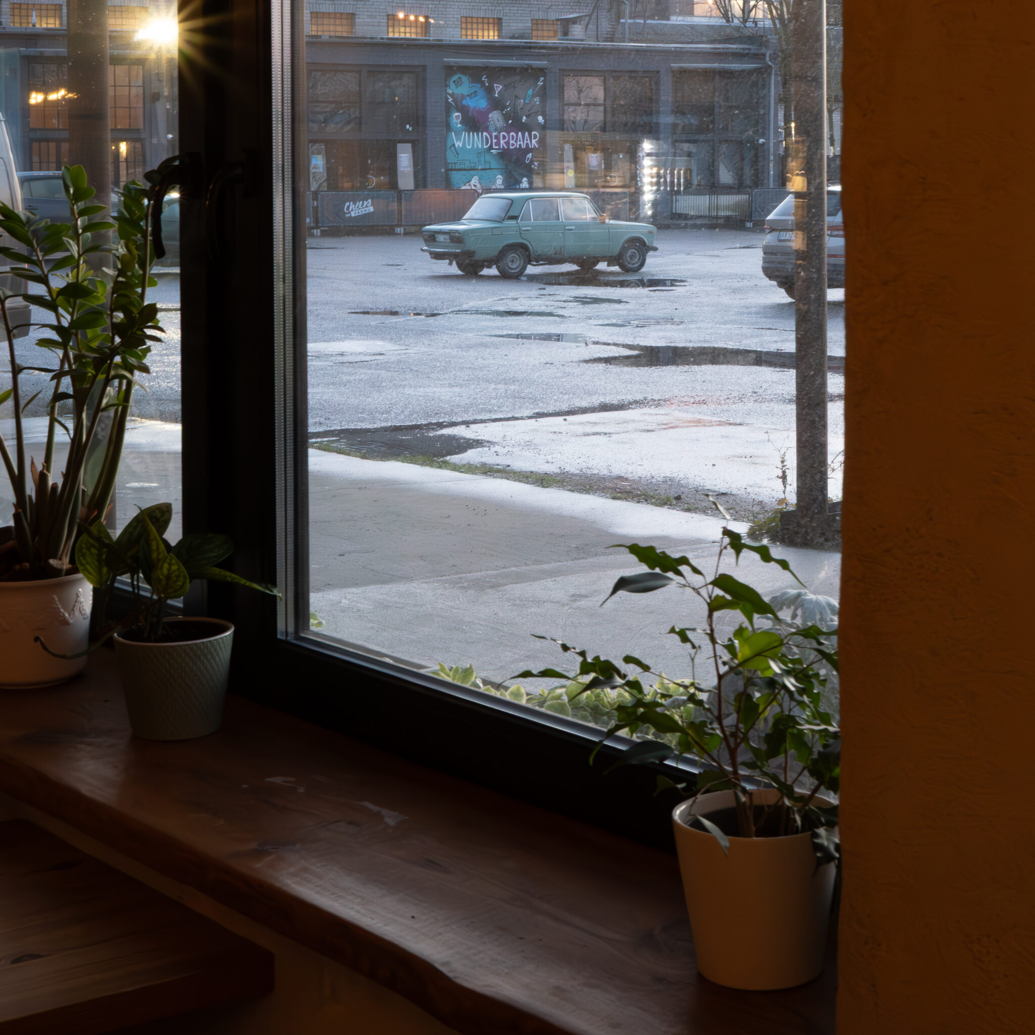 Vaade aknast tänavale, kus on vana auto ja taimed.