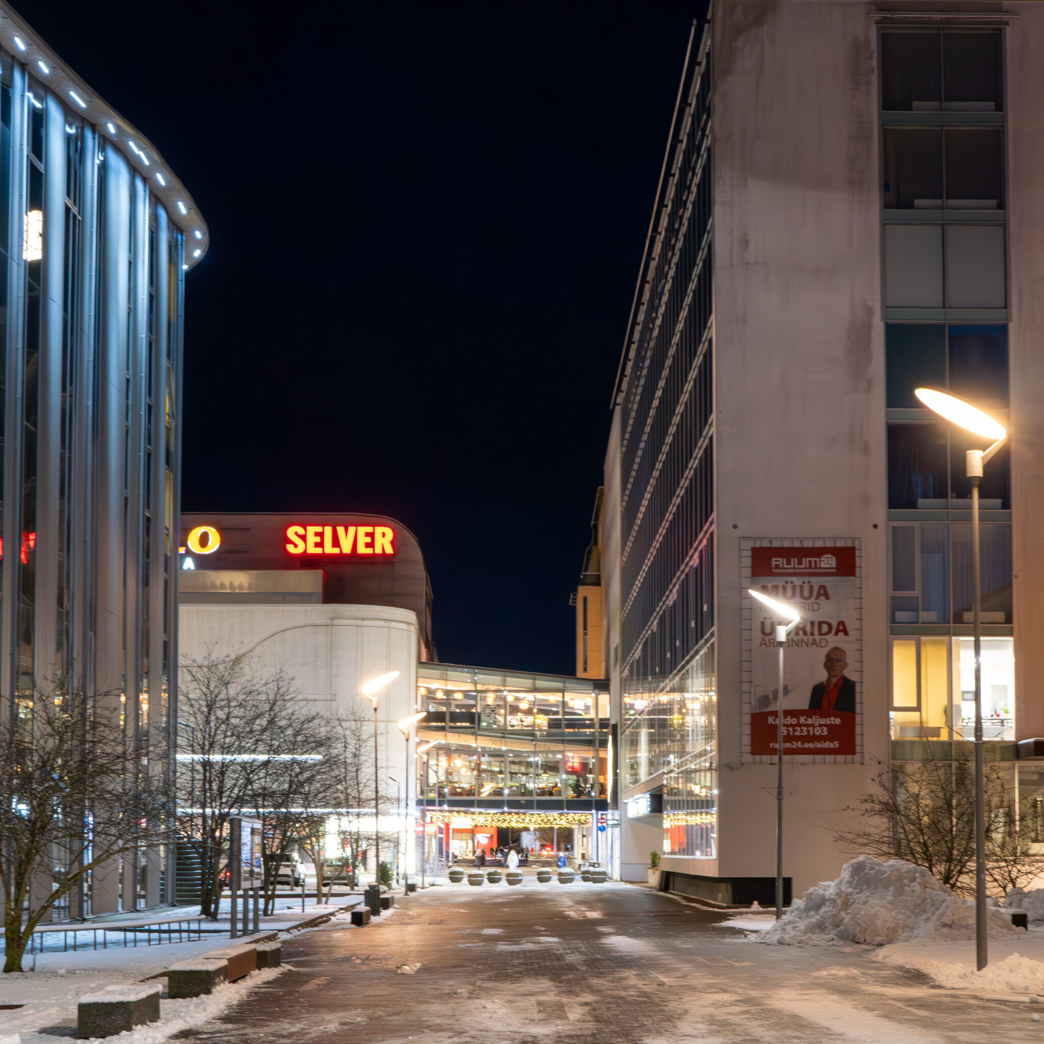 Lumine öine tänav valgustatud hoonete ja Selveri sildiga.