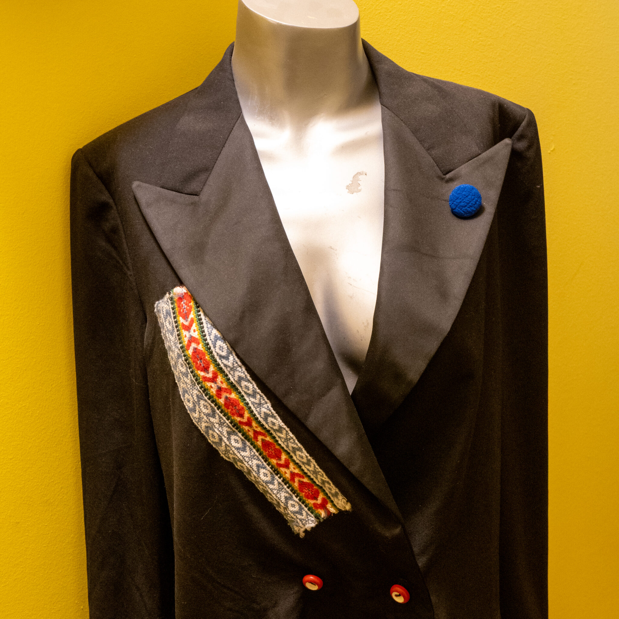 Mannekeen musta pintsaku, värvilise embleemi ja sinise nööbiga.