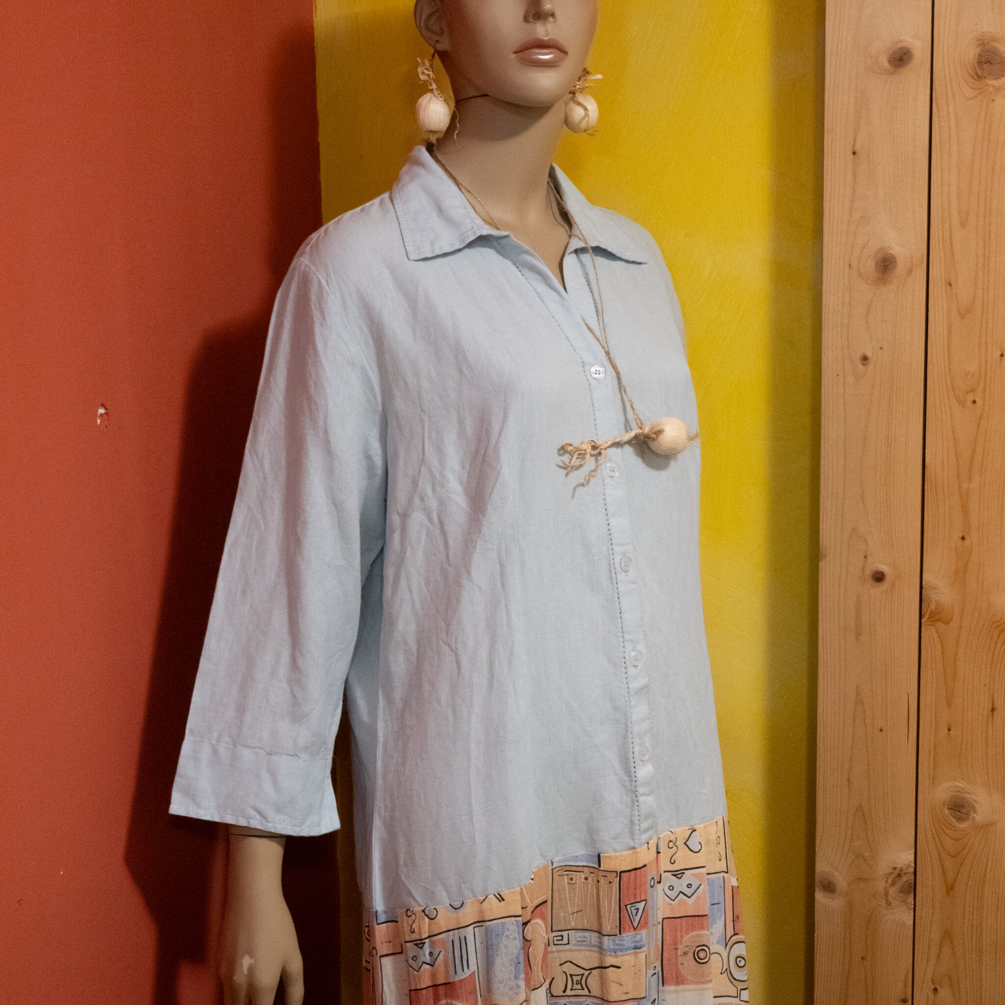 Mannekeen helesinises särgis, küüslaugukujuliste kõrvarõngaste ja värvilise seelikuga.