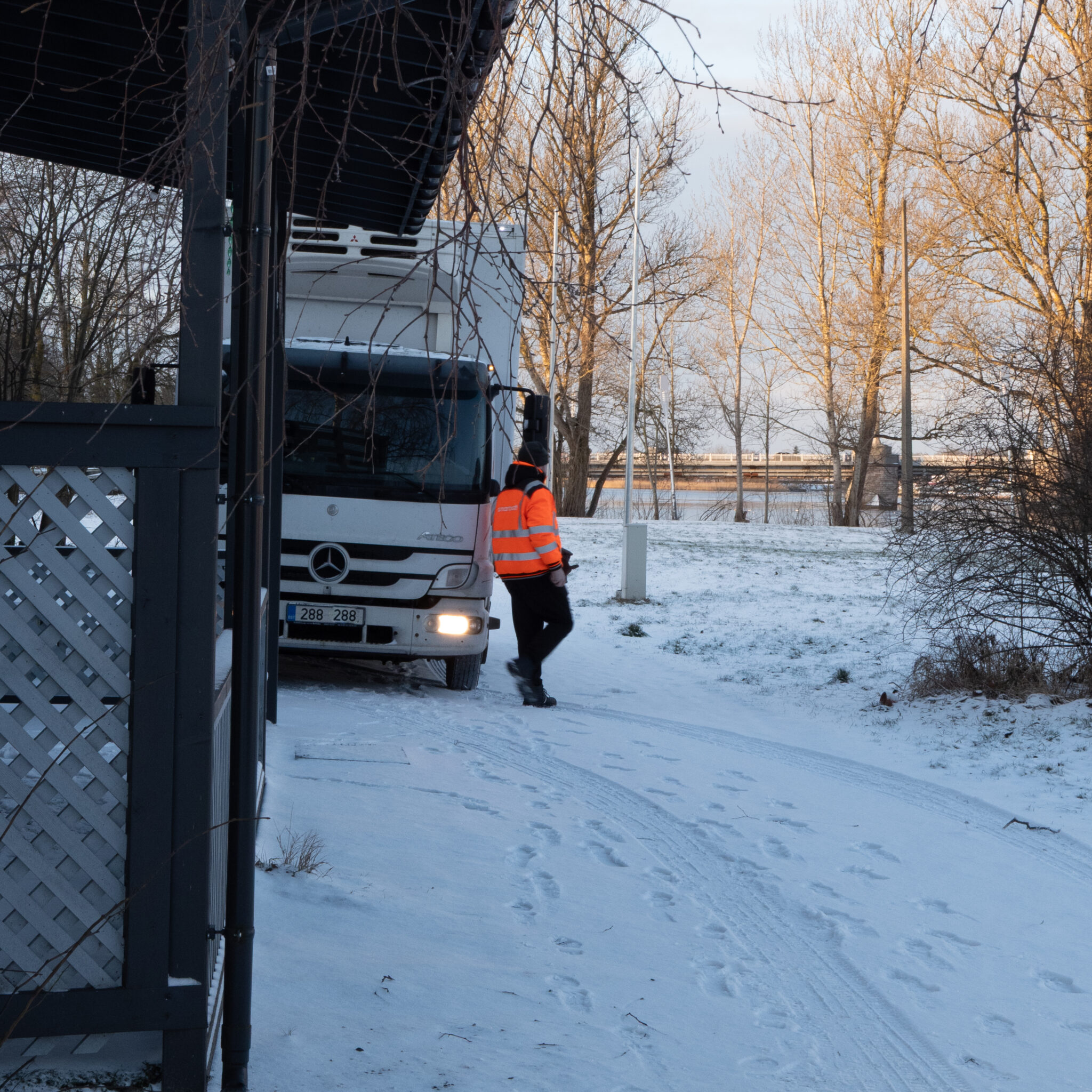 Helkurvestis inimene seisab veoauto kõrval lumistes oludes.