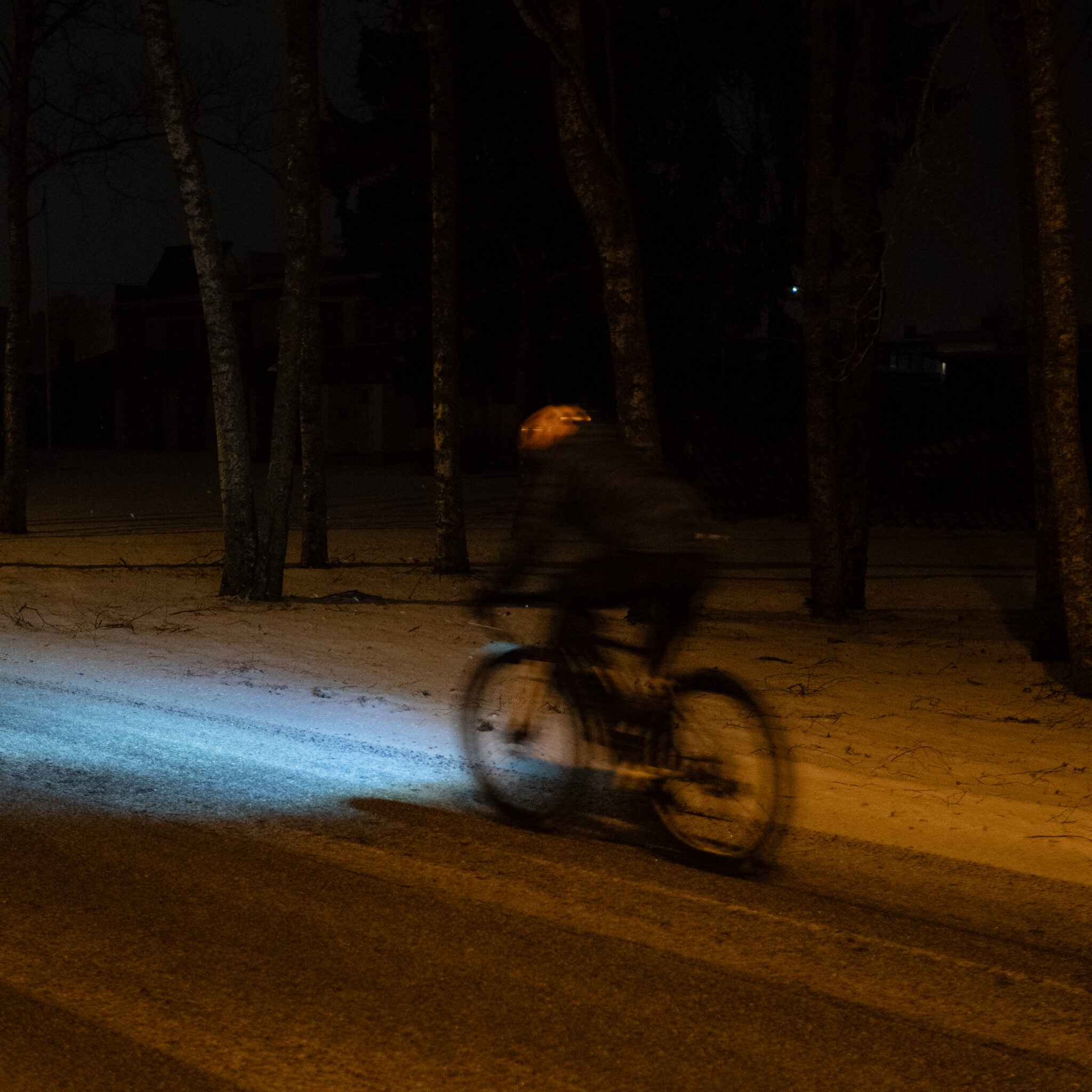 Jalgrattur sõidab öösel lumisel rajal esitule valguses.