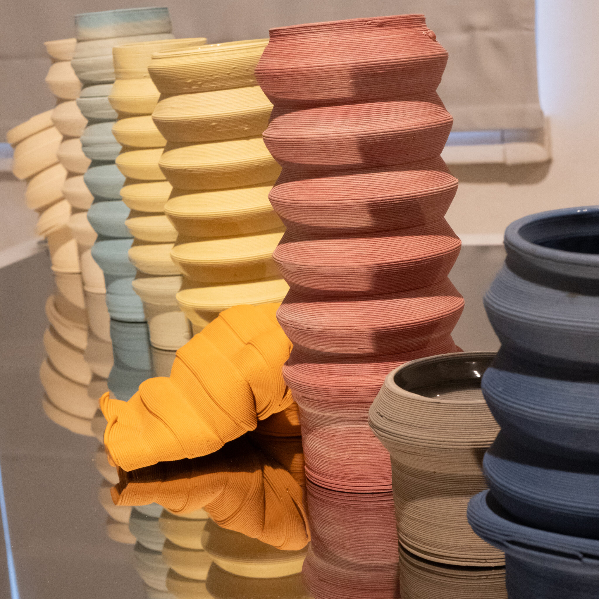 Rida värvilisi keraamilisi vaase peegeldaval pinnal.