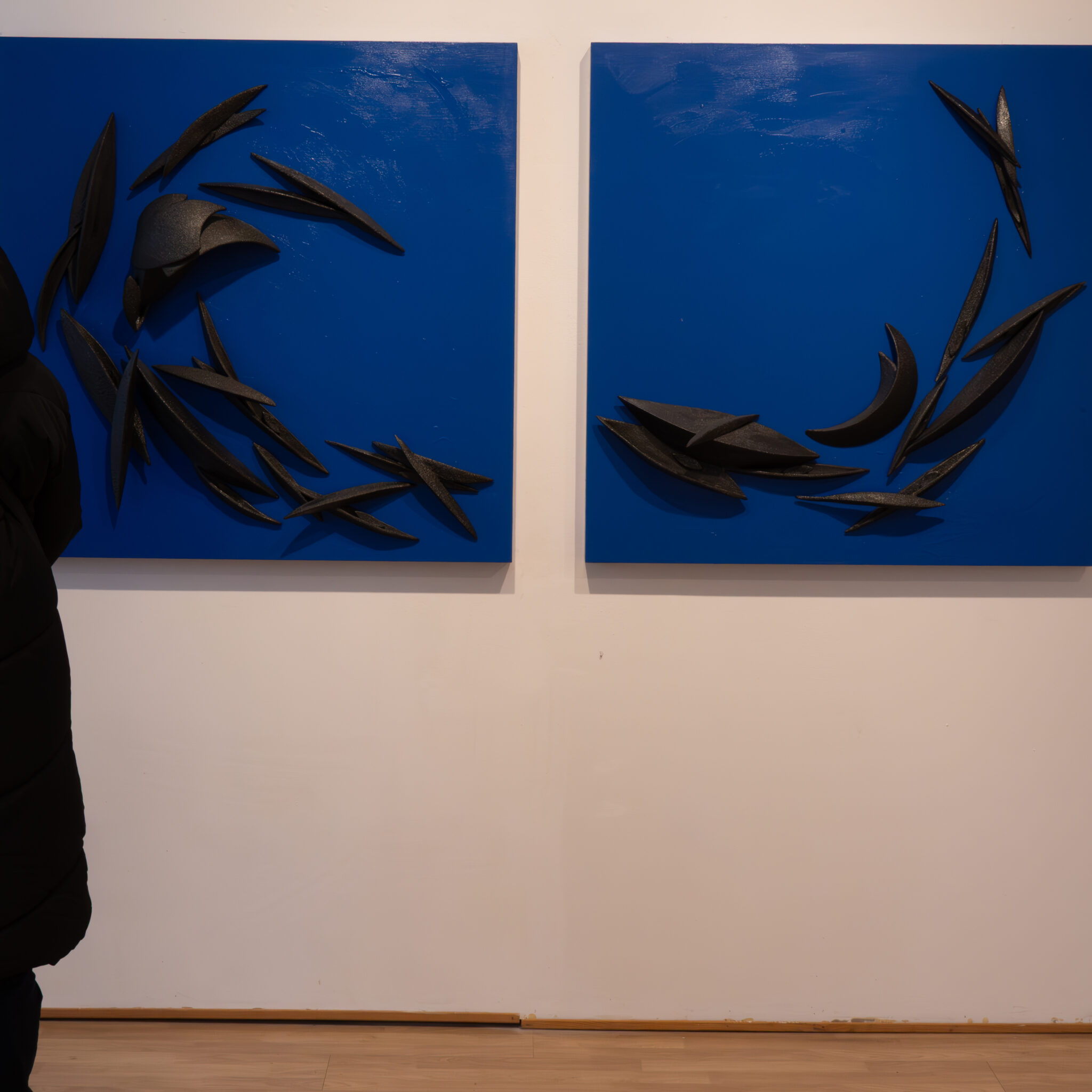 Kaks sinist maali mustade abstraktsete kujunditega valgel seinal.