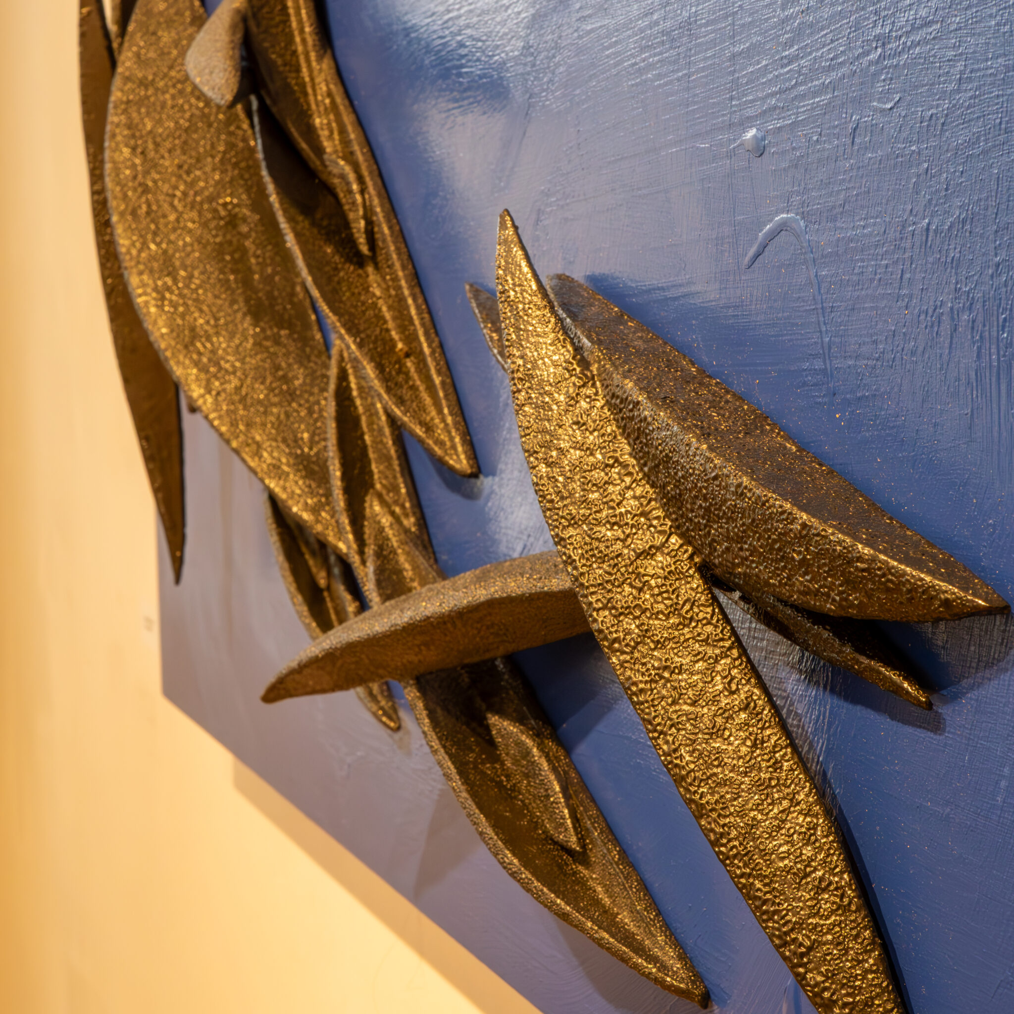 Metalliline abstraktne skulptuur sinise tausta ja kuldsete aktsentidega.