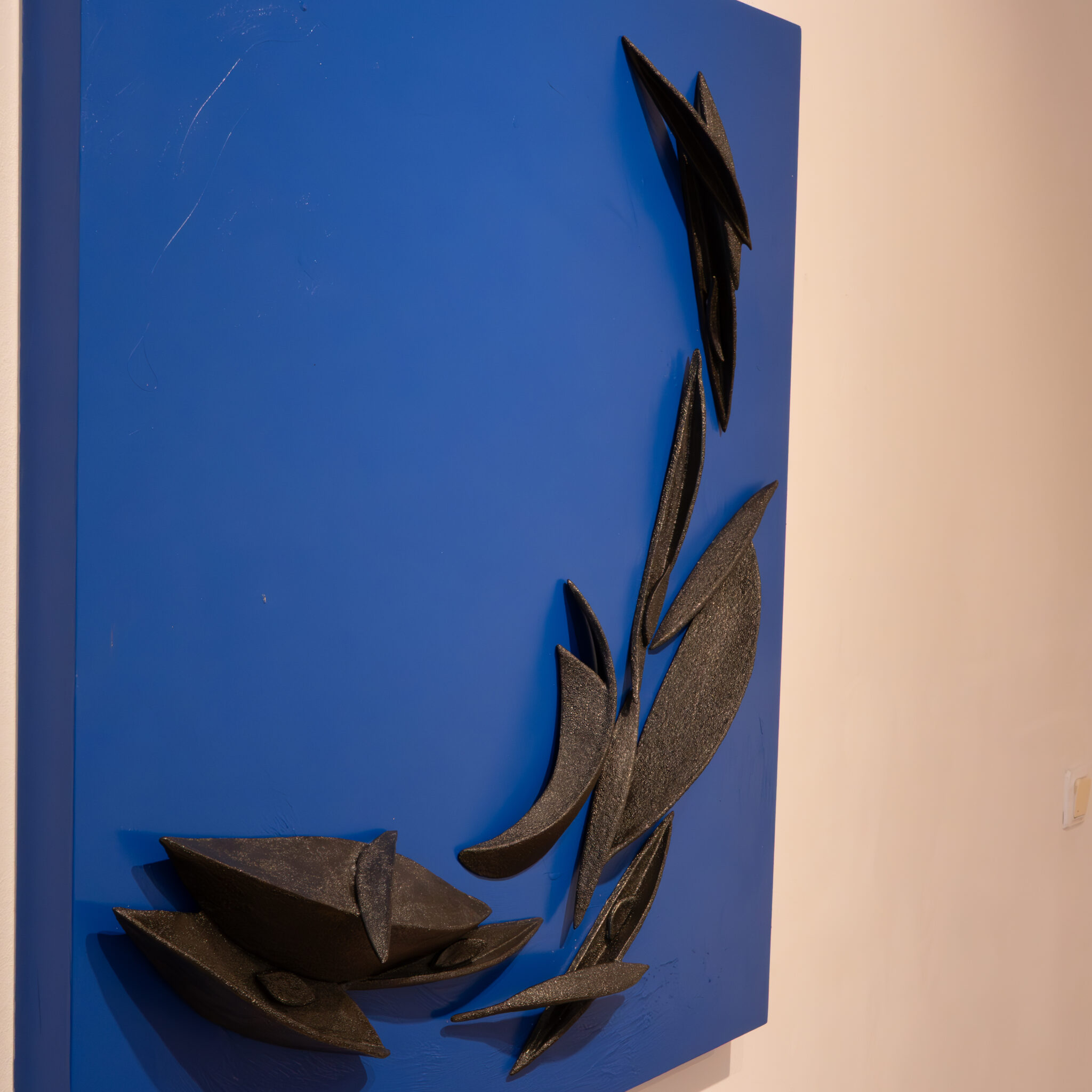 Sinimust abstraktne skulptuur ripub seinal.