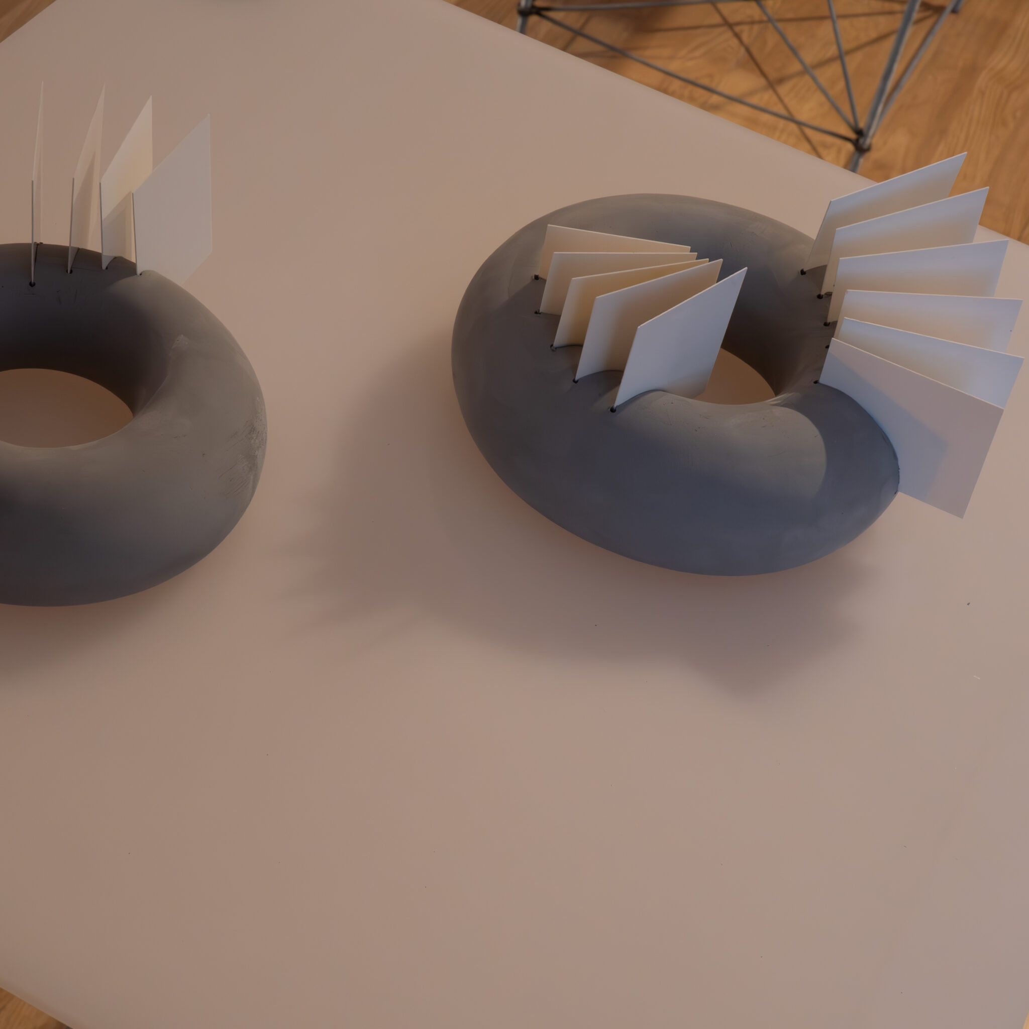 Kaks halli sõõrikukujulist objekti valgete pabervoltidega laual.