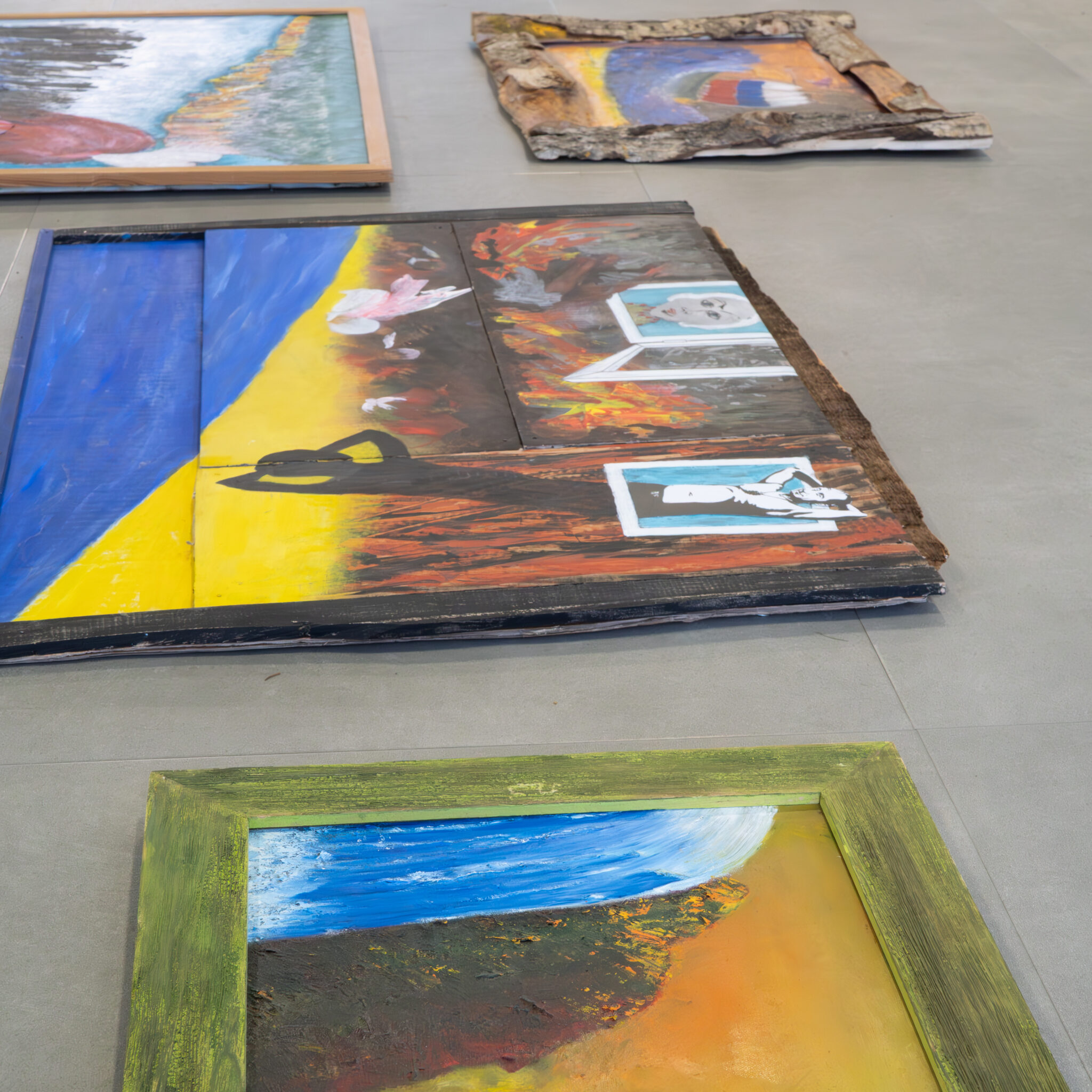 Põrandal eksponeeritud kunstiteosed, sealhulgas abstraktsed maalid ja puidust skulptuur.